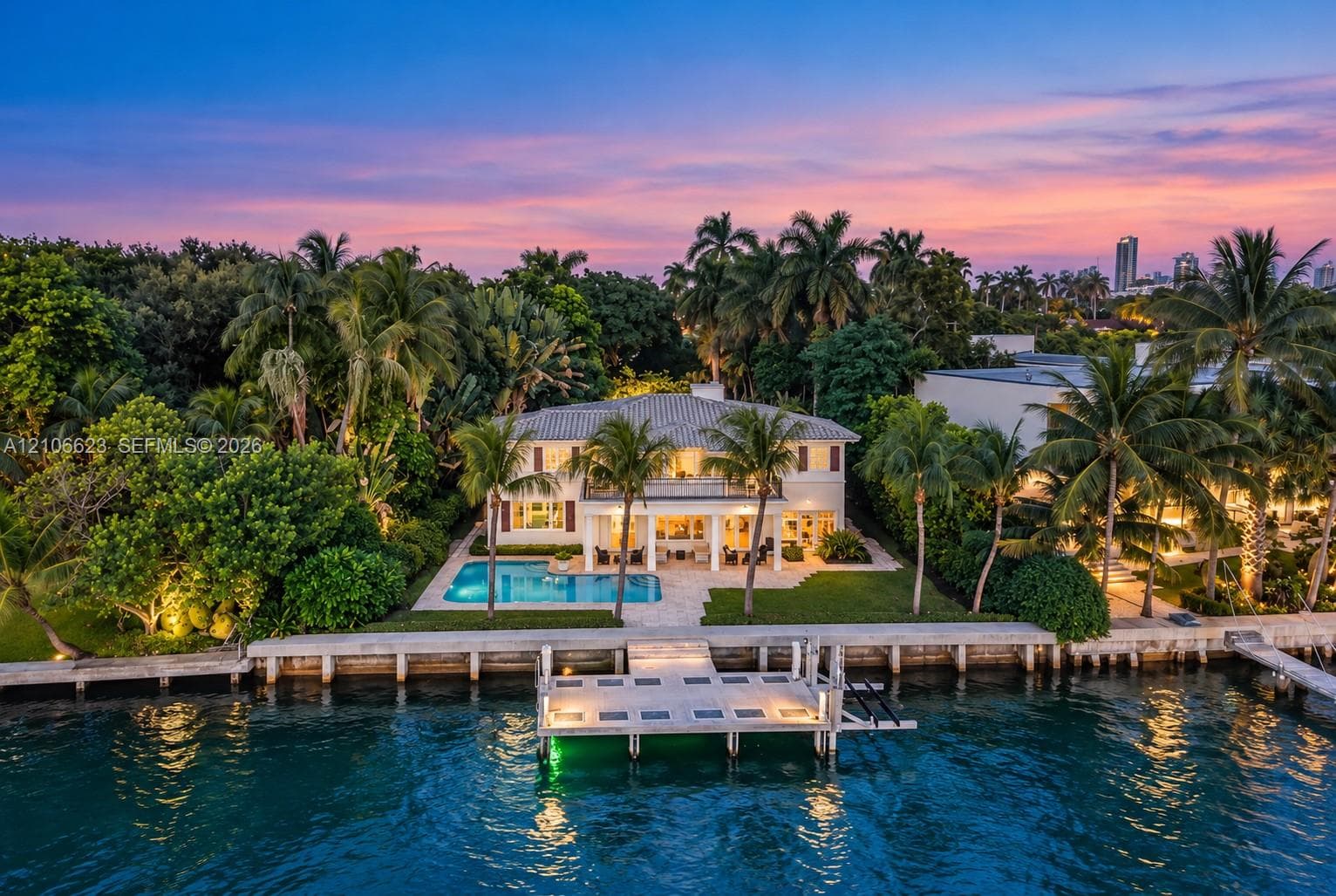 Waterfront estate featuring a private dock, swimming pool, two-story covered loggia, and landscaped grounds with mature palm trees