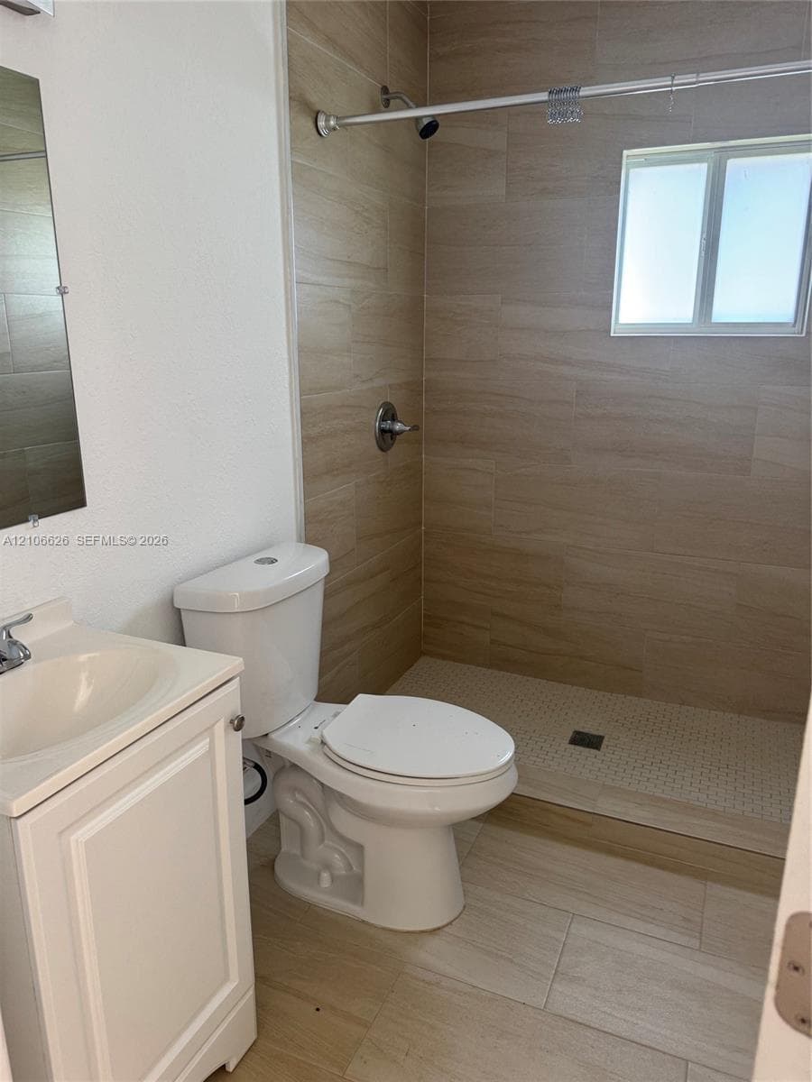 Bathroom featuring a vanity with an integrated sink, polished chrome faucet, tile-surround shower with a built-in bench, and light-toned tile flooring