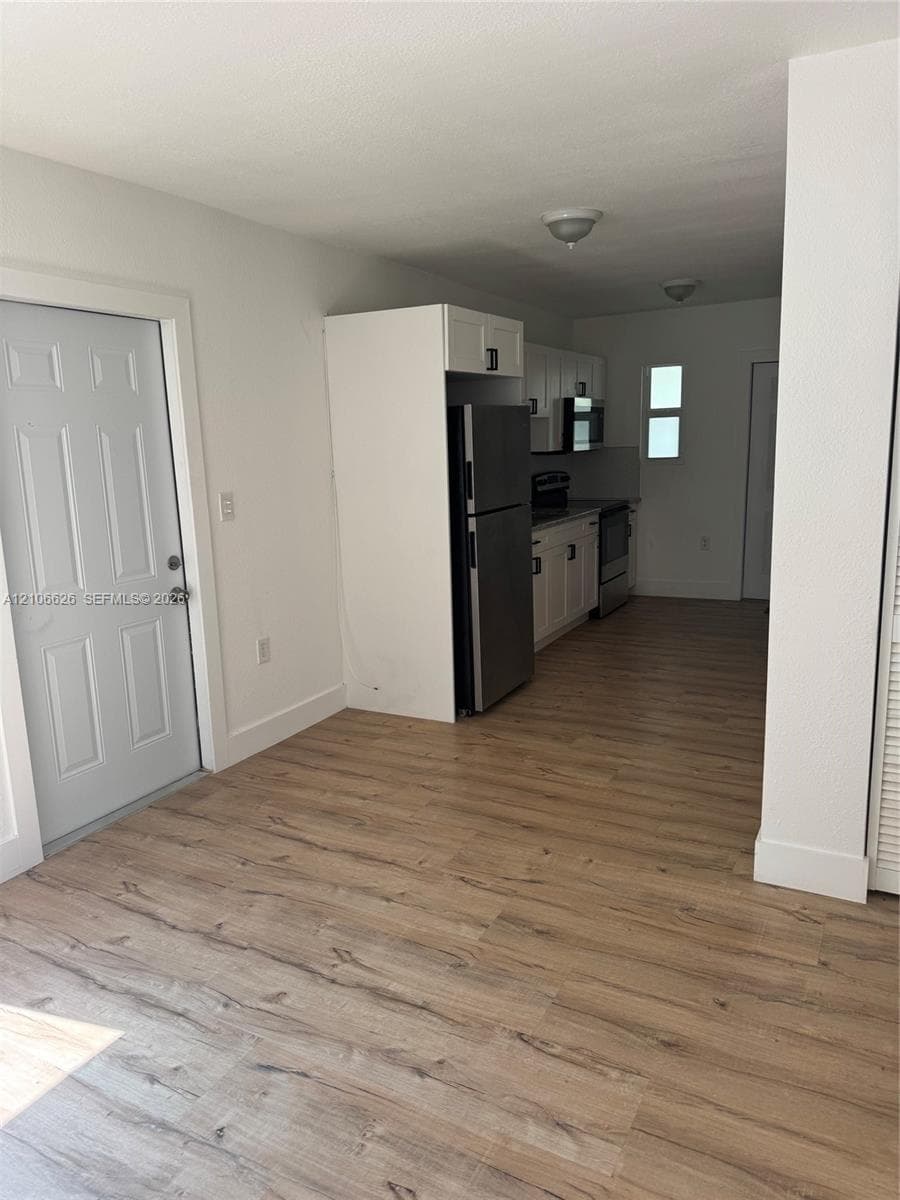 Kitchen featuring wood-finish flooring, white cabinetry, stainless steel refrigerator, and recessed ceiling lighting