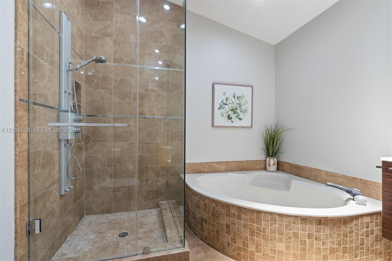Walk-in shower with stone tile surround, frameless glass enclosure, and wall-mounted shower panel, paired with a corner soaking tub featuring a stone tile skirt and matching deck