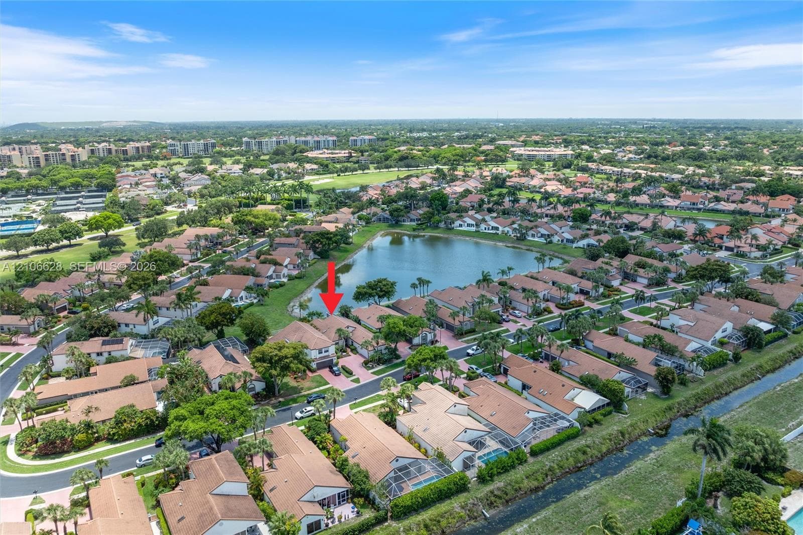 Aerial perspective of a multi-story residence featuring a paved driveway, tile roof, and waterfront location within a residential community