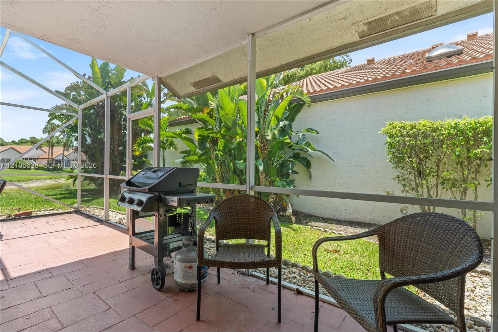 Screen-enclosed patio featuring masonry tile flooring, metal frame construction, and direct access to an outdoor area with mature vegetation