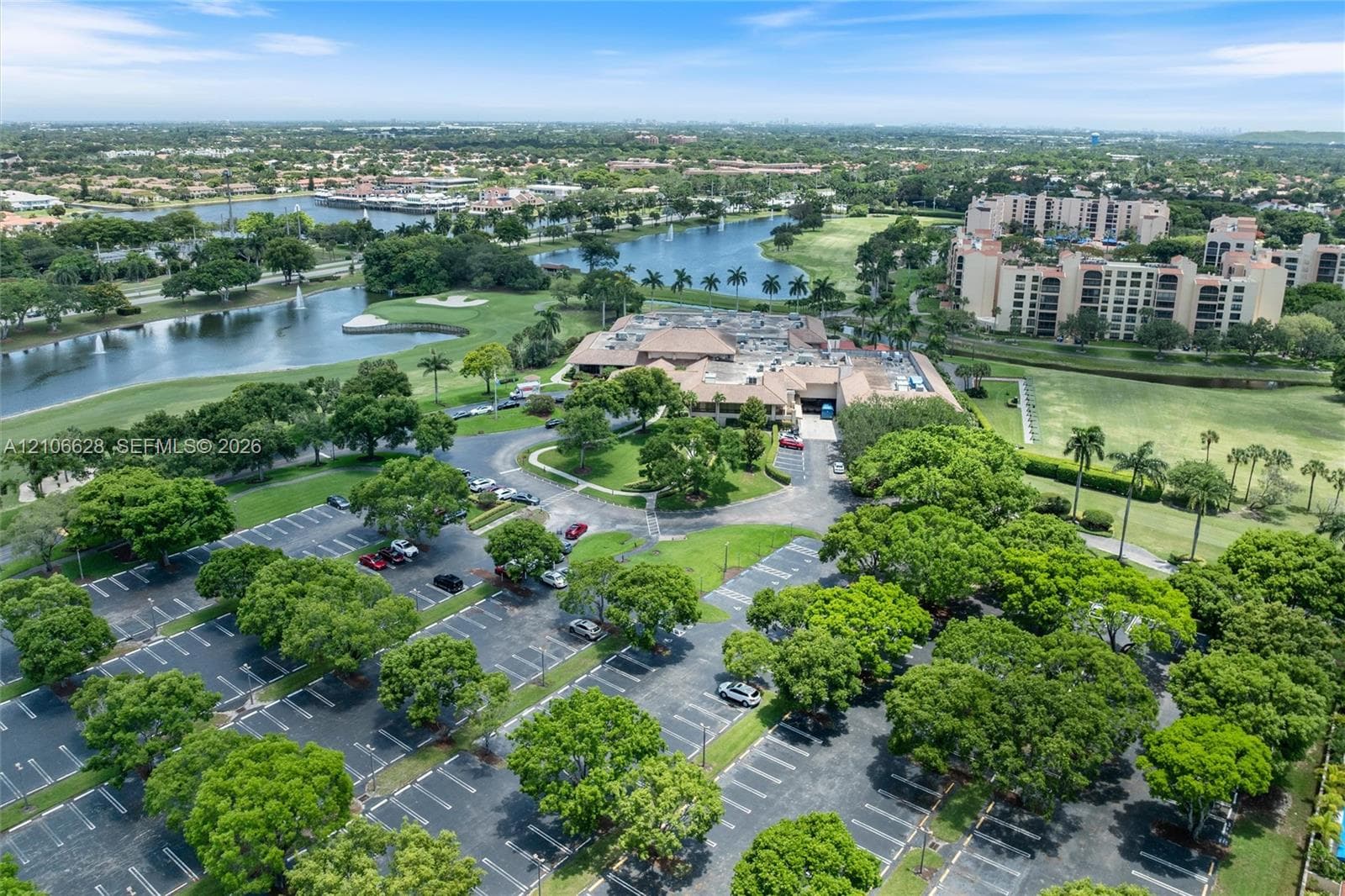 Aerial perspective featuring mature landscaping, paved surface parking, multi-story buildings, and water features