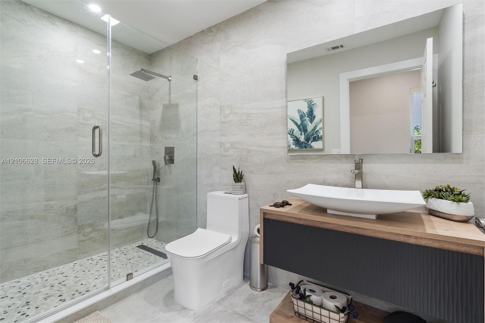 Floating vanity with a vessel sink and wood-finish countertop, glass-enclosed shower with a rainfall showerhead, and wall-to-wall stone-finish tile