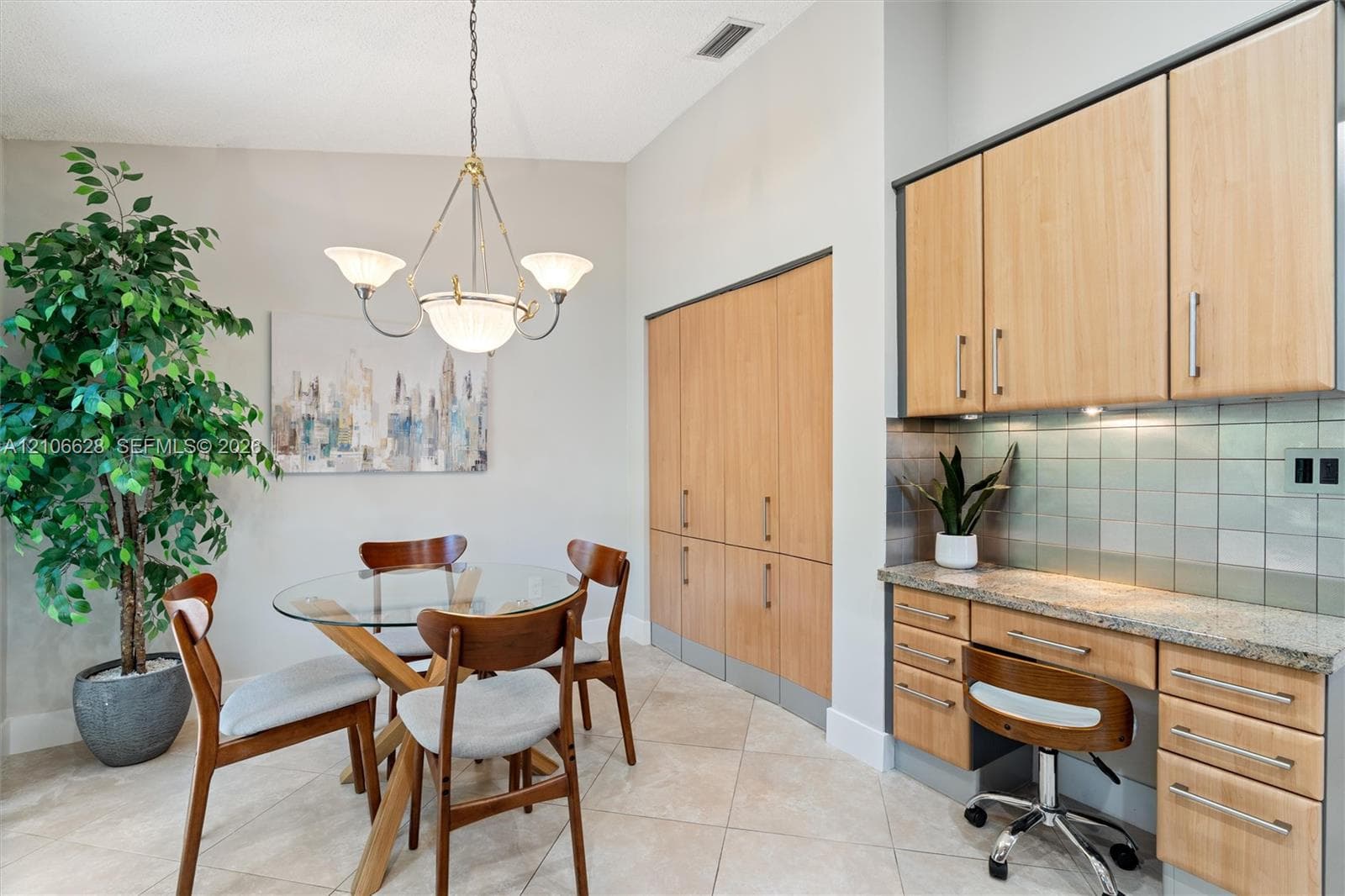 Built-in light-tone cabinetry, stone countertop workspace, tiled backsplash, and decorative multi-arm chandelier