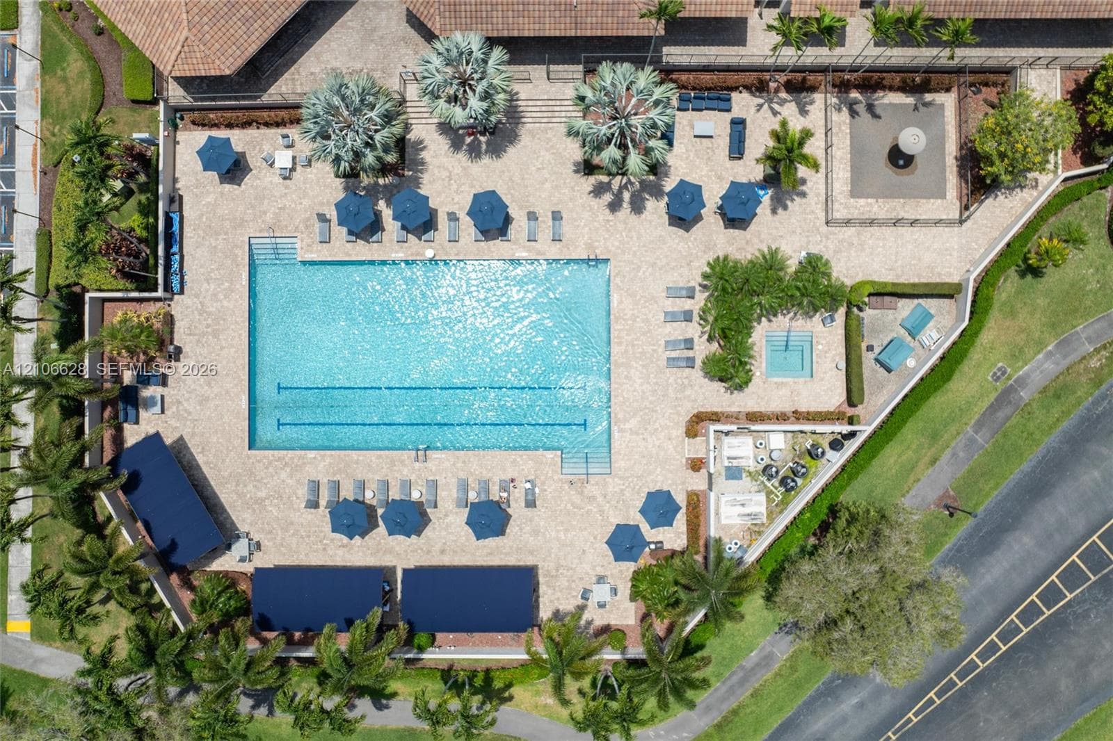 Aerial view of a swimming pool complex featuring a lap lane configuration, an integrated spa, paved pool deck, and shaded structures