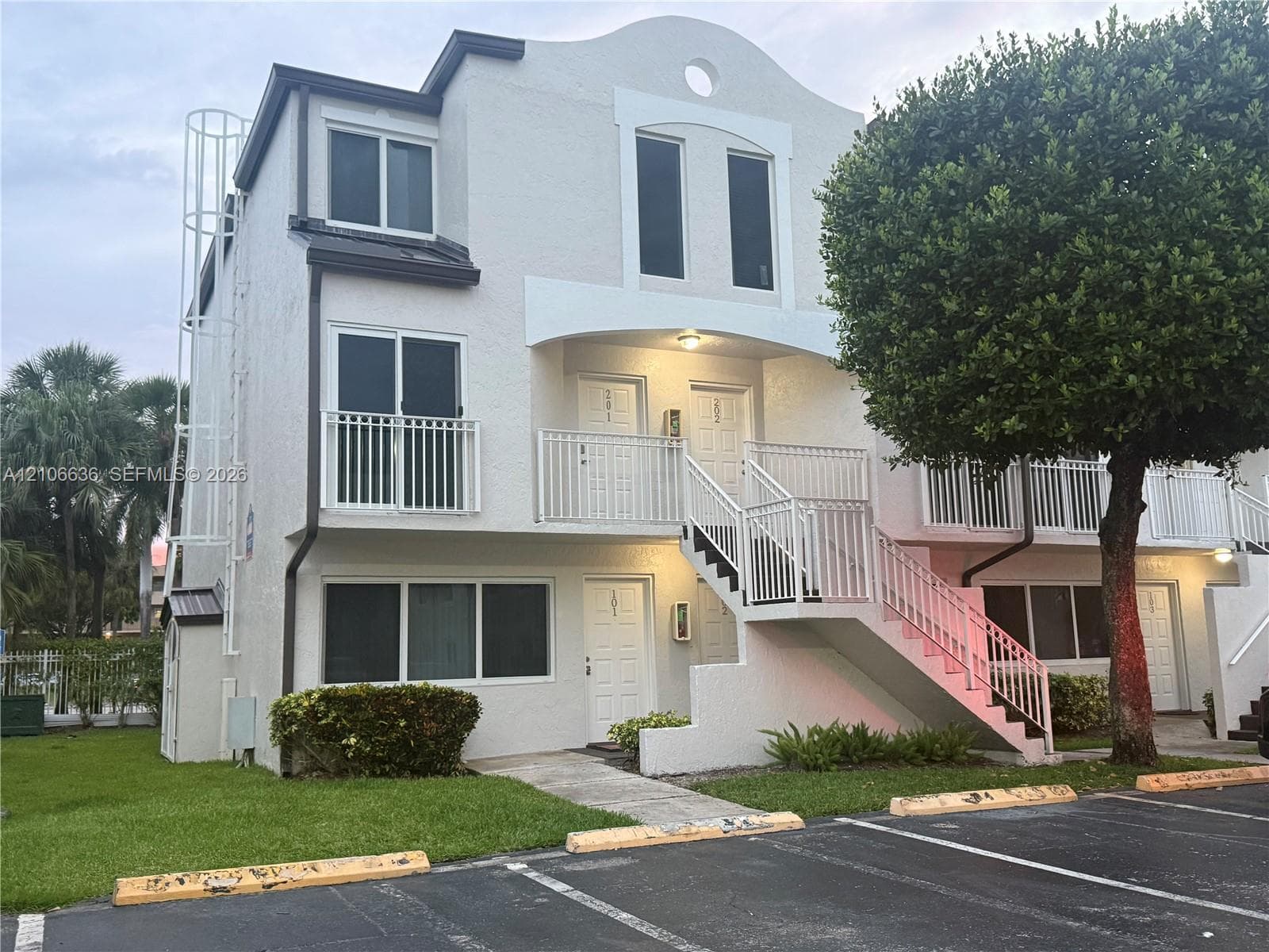 Multi-story exterior featuring light-toned stucco facade, arched roofline detail, private balconies with white railings, and integrated exterior staircase