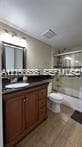 Bathroom vanity with wood-finish cabinetry, dark solid-surface countertop, oval undermount sink, and glass-enclosed shower