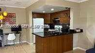 Kitchen featuring wood cabinetry, dark stone countertops, integrated breakfast bar, and recessed lighting