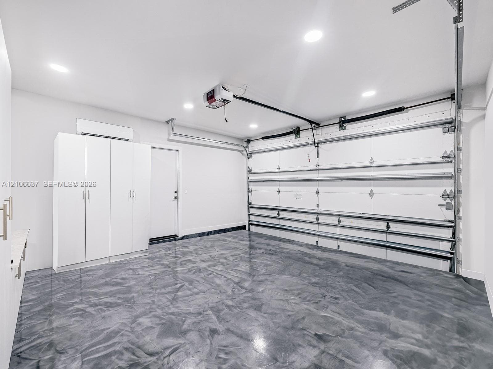 Garage featuring high-gloss epoxy flooring, built-in white cabinetry, recessed LED lighting, and a climate control unit