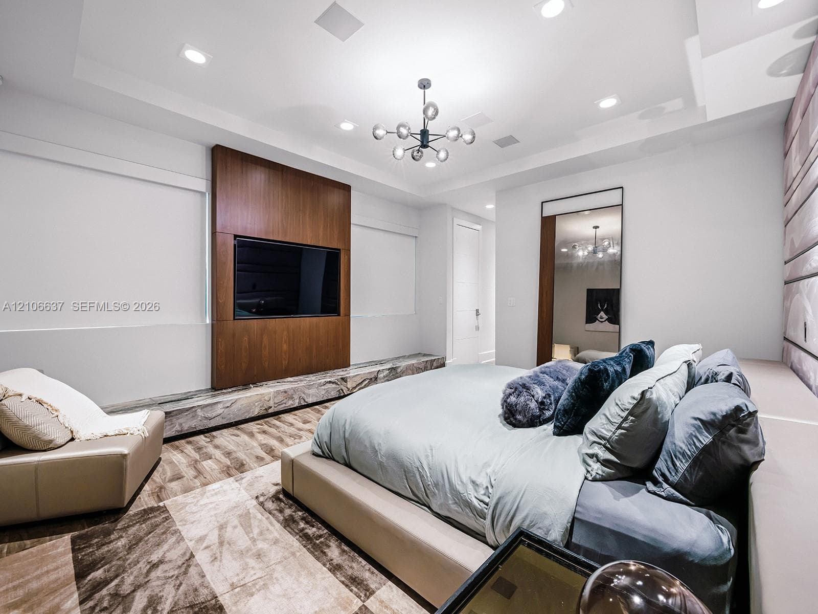 Tray ceiling with recessed lighting, central multi-arm modern light fixture, wood-finish media wall with stone hearth, and floor-to-ceiling mirror