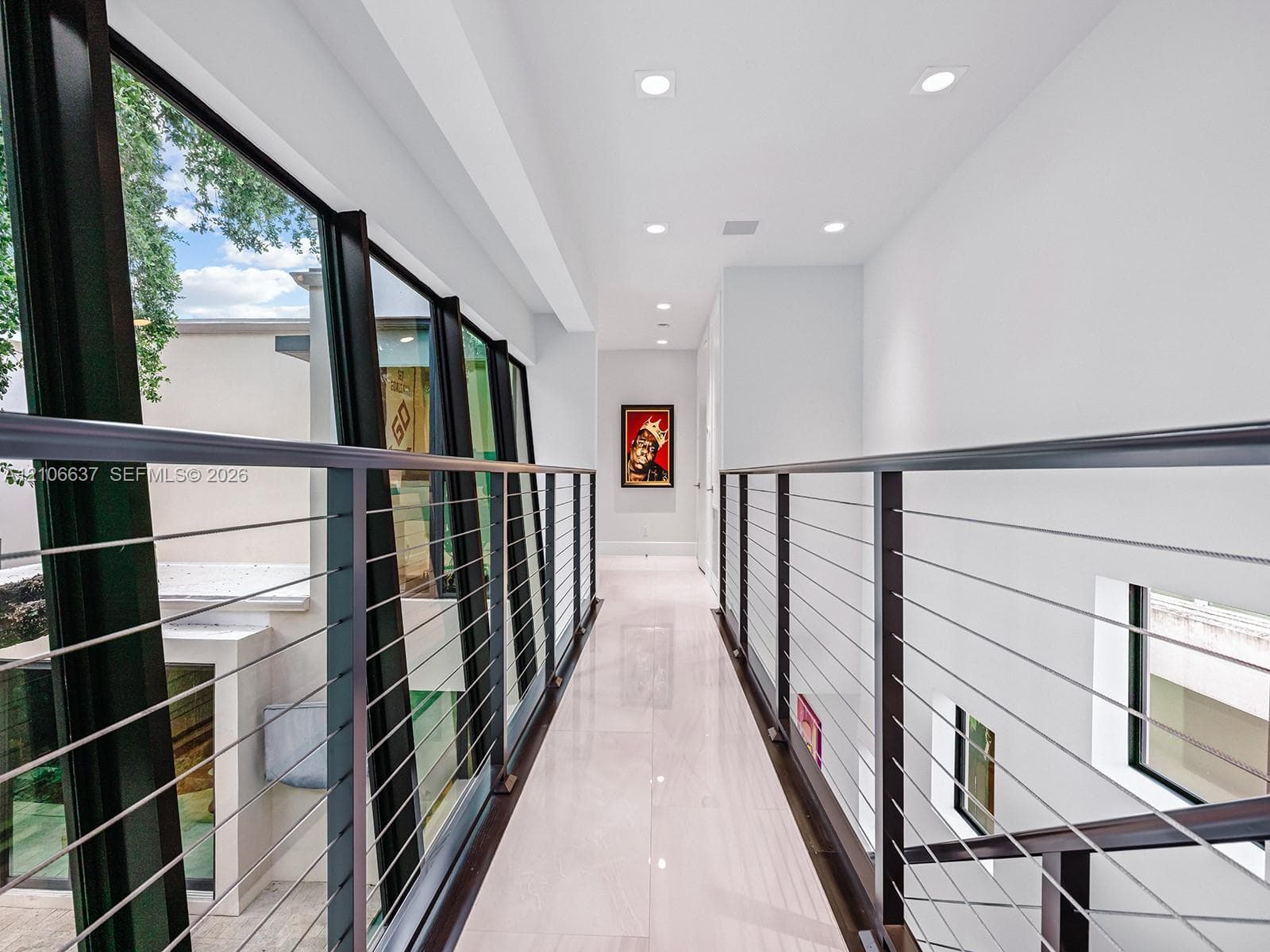 Hallway featuring polished light-toned flooring, recessed ceiling lighting, and a metal cable railing system with dark-finish posts, complemented by floor-to-ceiling glass paneling