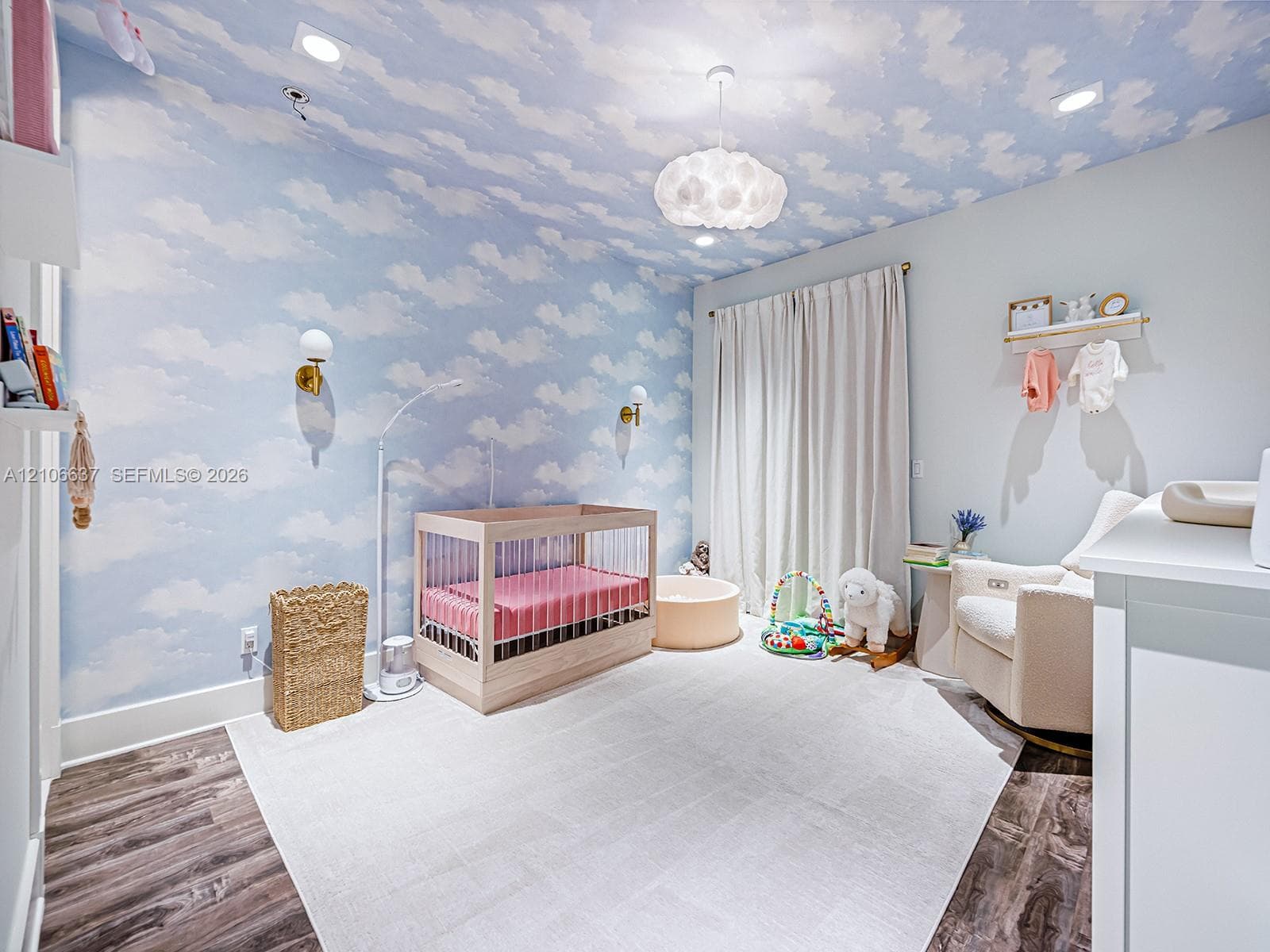 Room featuring cloud-patterned wallpaper extending to the ceiling, wood-finish flooring, dual wall-mounted brass light fixtures, recessed ceiling lighting, and a textured sphere pendant light