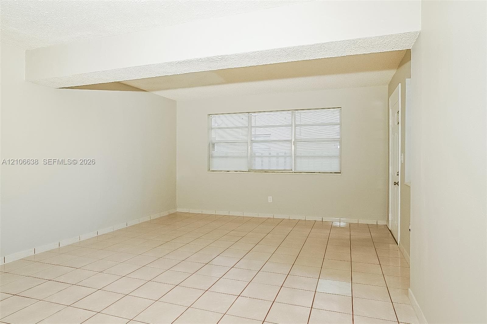 Neutral interior space featuring tiled flooring, textured ceiling, and a multi-panel window with integrated blinds