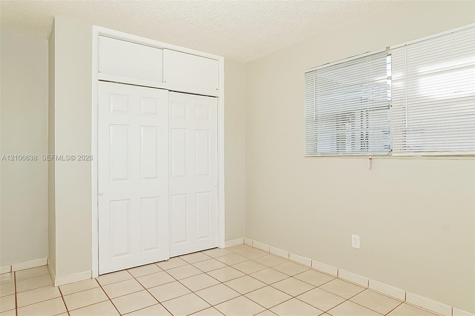 Room featuring tile flooring, neutral wall tones, and a built-in sliding closet with overhead storage compartments