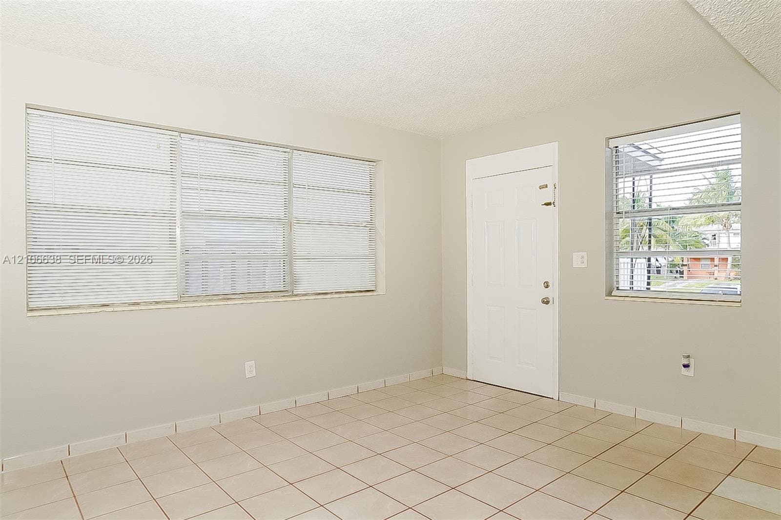 Neutral-toned interior space featuring light-colored ceramic tile flooring, a multi-panel exterior entry door, and large horizontal sliding windows with integrated blinds