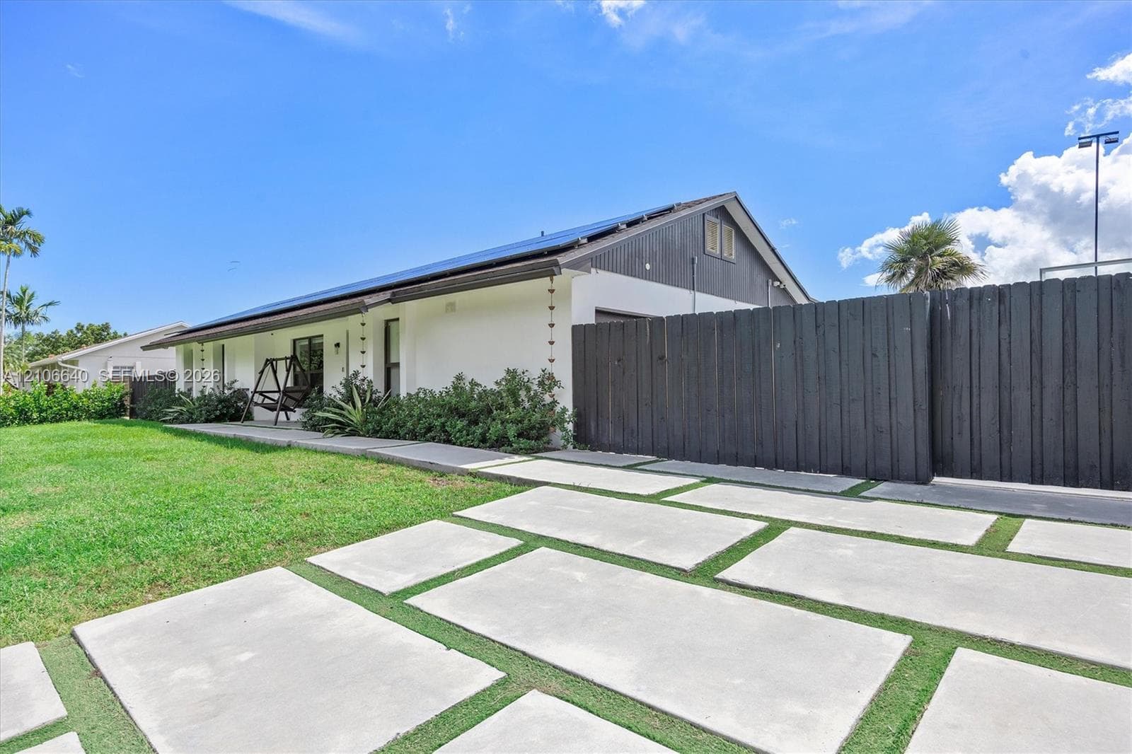 Single-story exterior featuring a grid-pattern concrete paver driveway, dark-tone vertical privacy fencing, and roof-mounted solar panels
