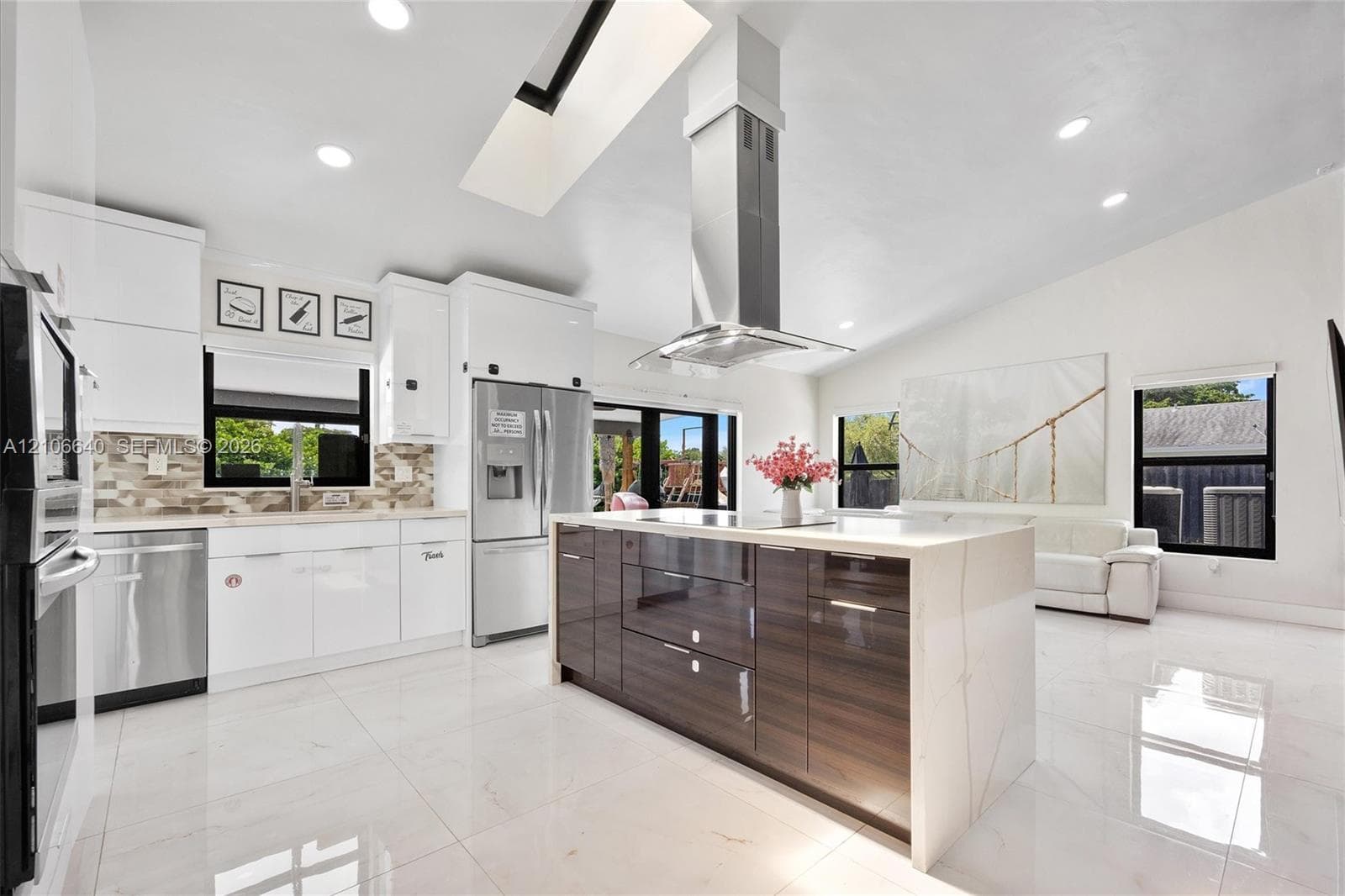 Modern kitchen featuring white cabinetry, stainless steel appliances, a center island with a wood-finish base, and vaulted ceilings with a skylight