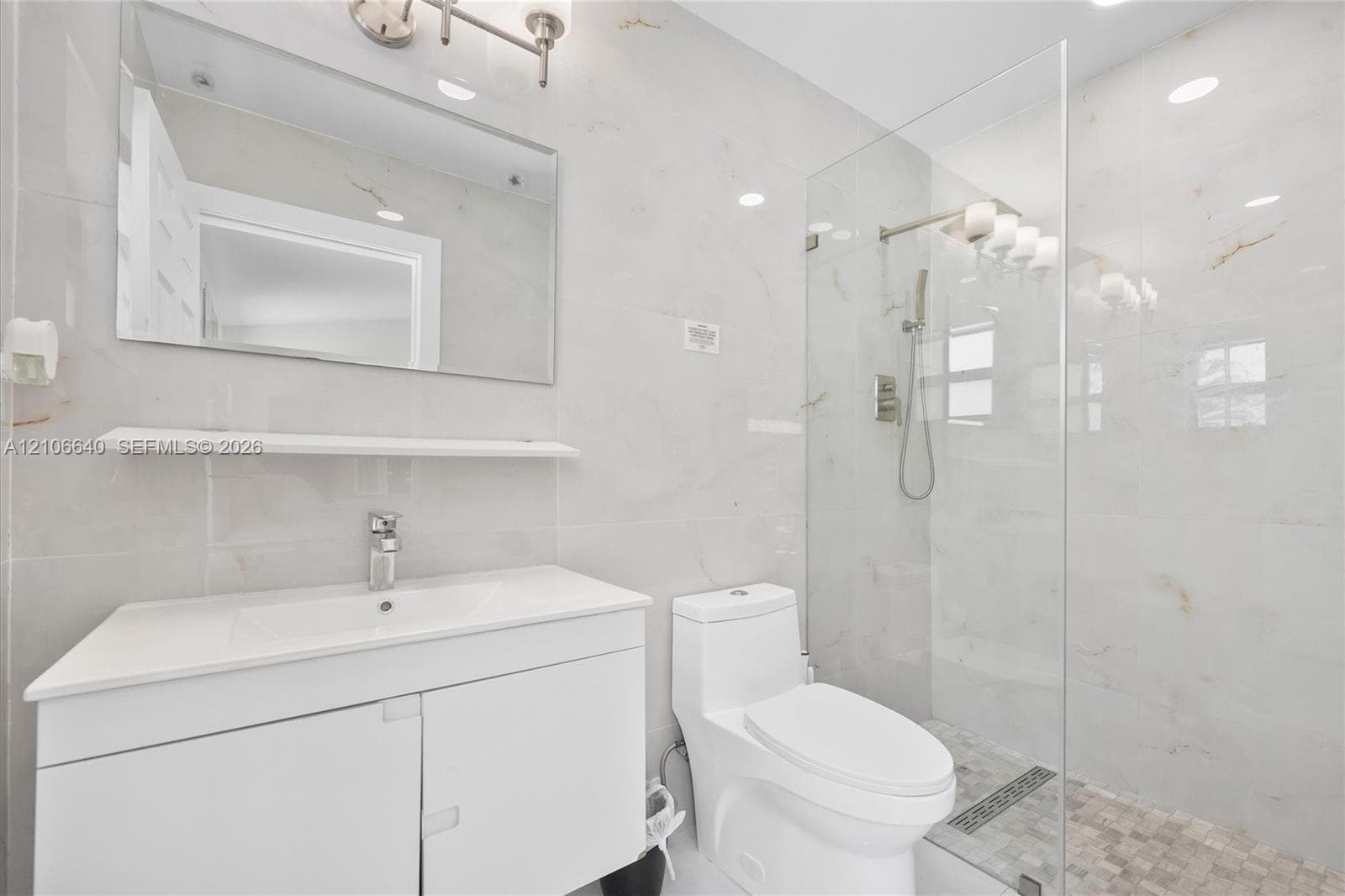 Bathroom featuring a glass-enclosed shower, wall-mounted shower system, white vanity with integrated sink, and white large-format wall tiles