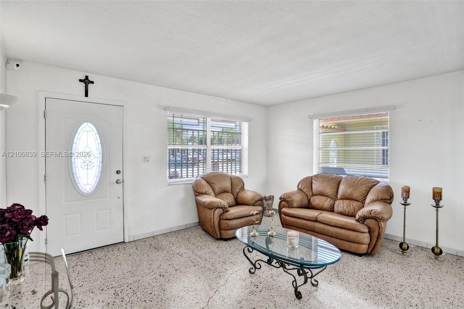 Interior space featuring polished terrazzo flooring, large windows with horizontal blinds, and a white entry door with an oval decorative glass insert