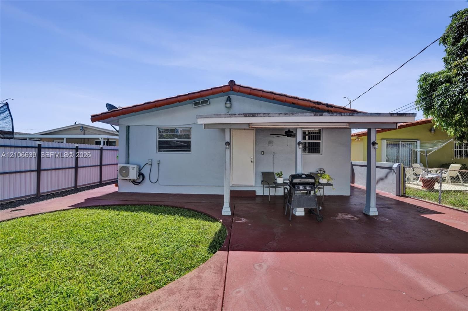 Covered rear patio featuring a painted concrete floor, tile roof, privacy fencing, and a manicured lawn