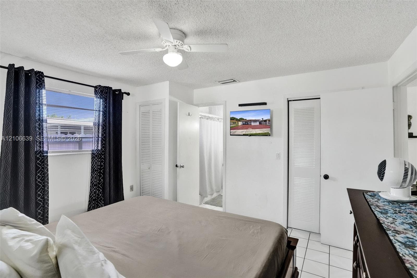 Bedroom featuring white tile flooring, ceiling fan with integrated lighting, and dual louvered-door closets