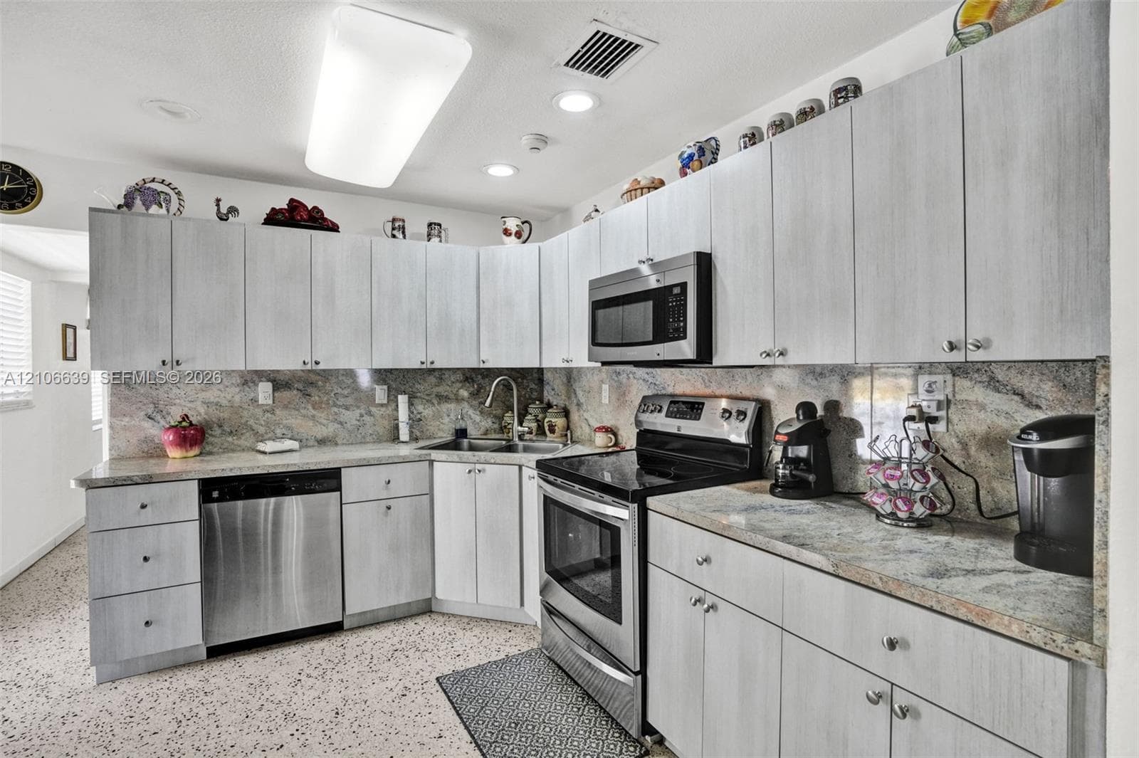 Kitchen featuring light-toned cabinetry, natural stone countertops with matching backsplash, stainless steel appliances, and integrated recessed lighting