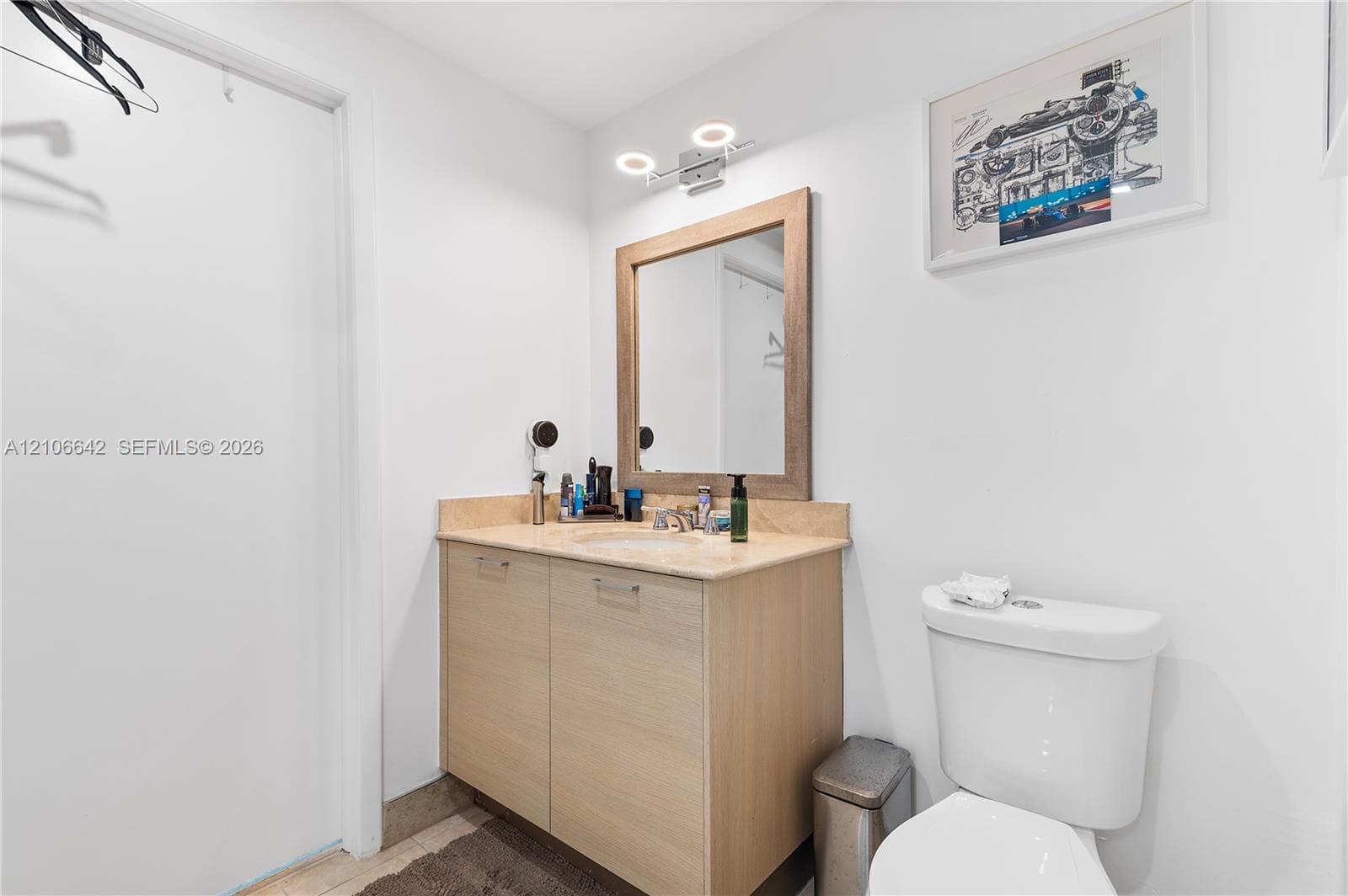 Vanity featuring wood-finish cabinetry, stone countertop with integrated sink, framed mirror, and dual-light fixture