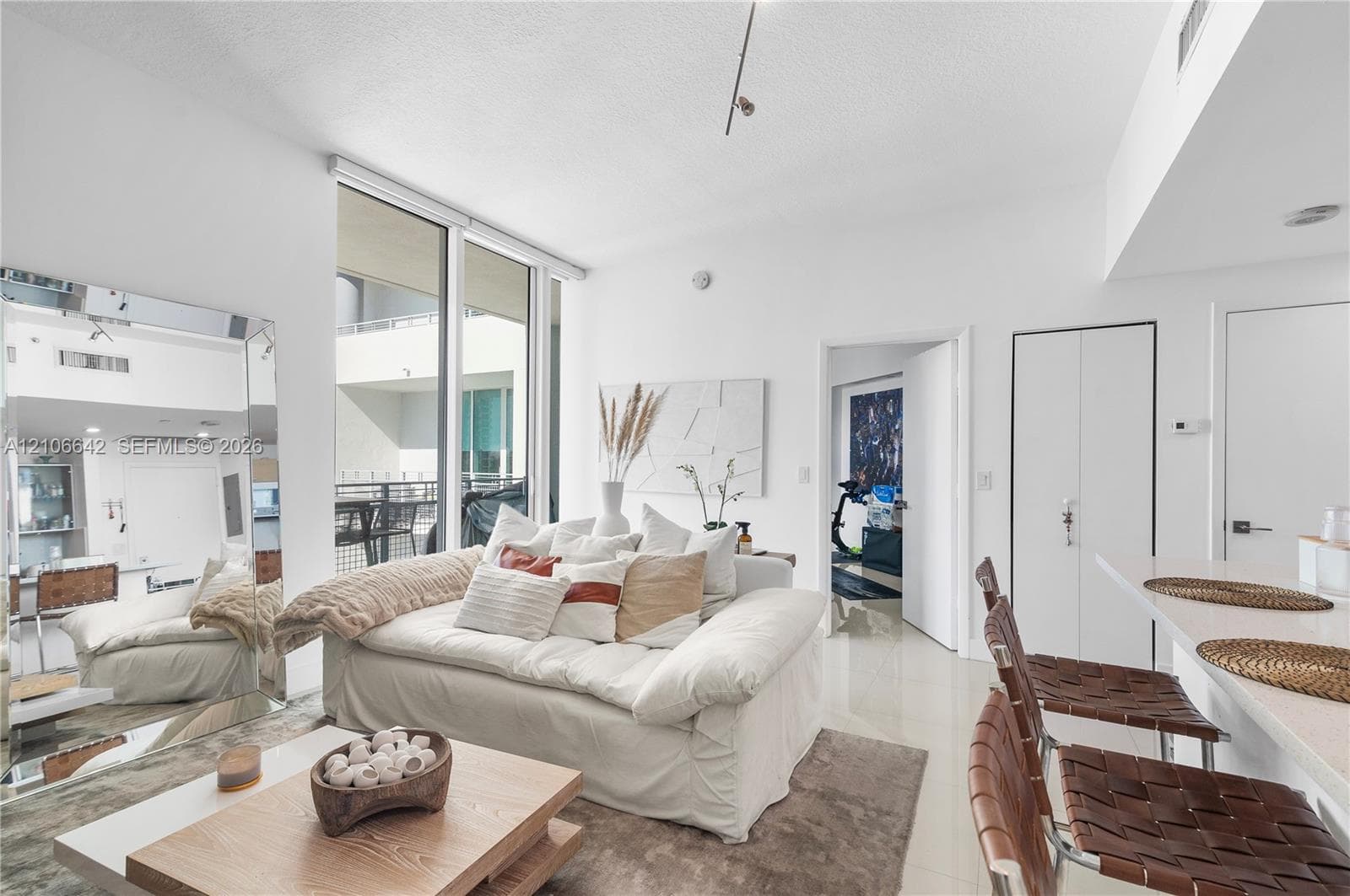 Open-concept living area featuring floor-to-ceiling windows, neutral tile flooring, track lighting, and a breakfast bar with stone-finish countertops