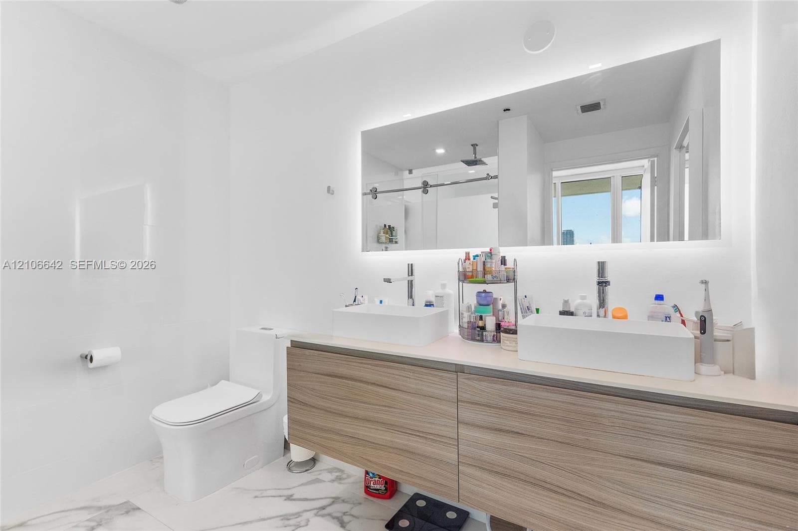 Floating vanity with wood-finish cabinetry, dual vessel sinks, quartz countertop, and a large backlit mirror