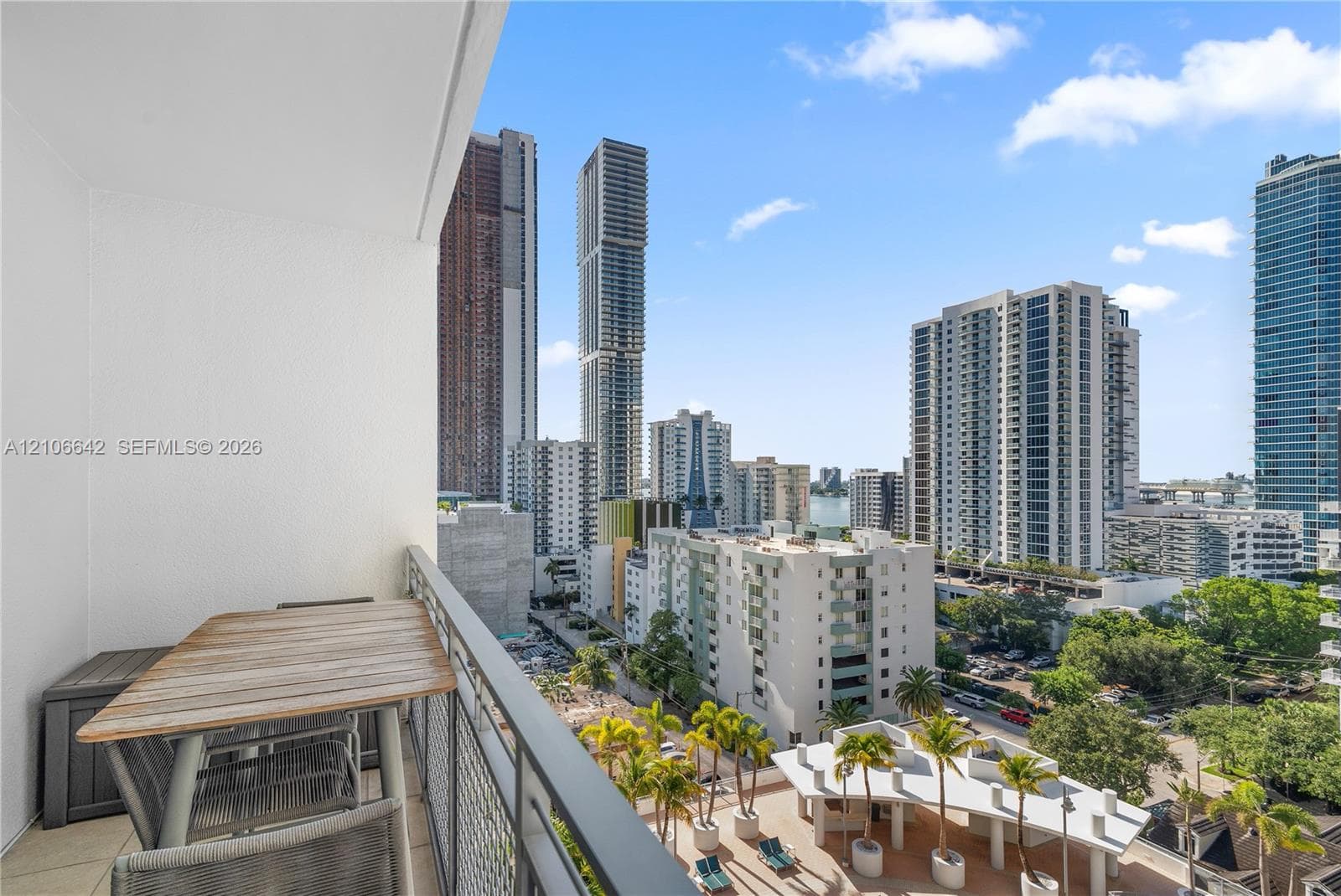 Private balcony featuring a metal railing and tile flooring, set against a backdrop of urban high-rise architecture and palm tree landscaping