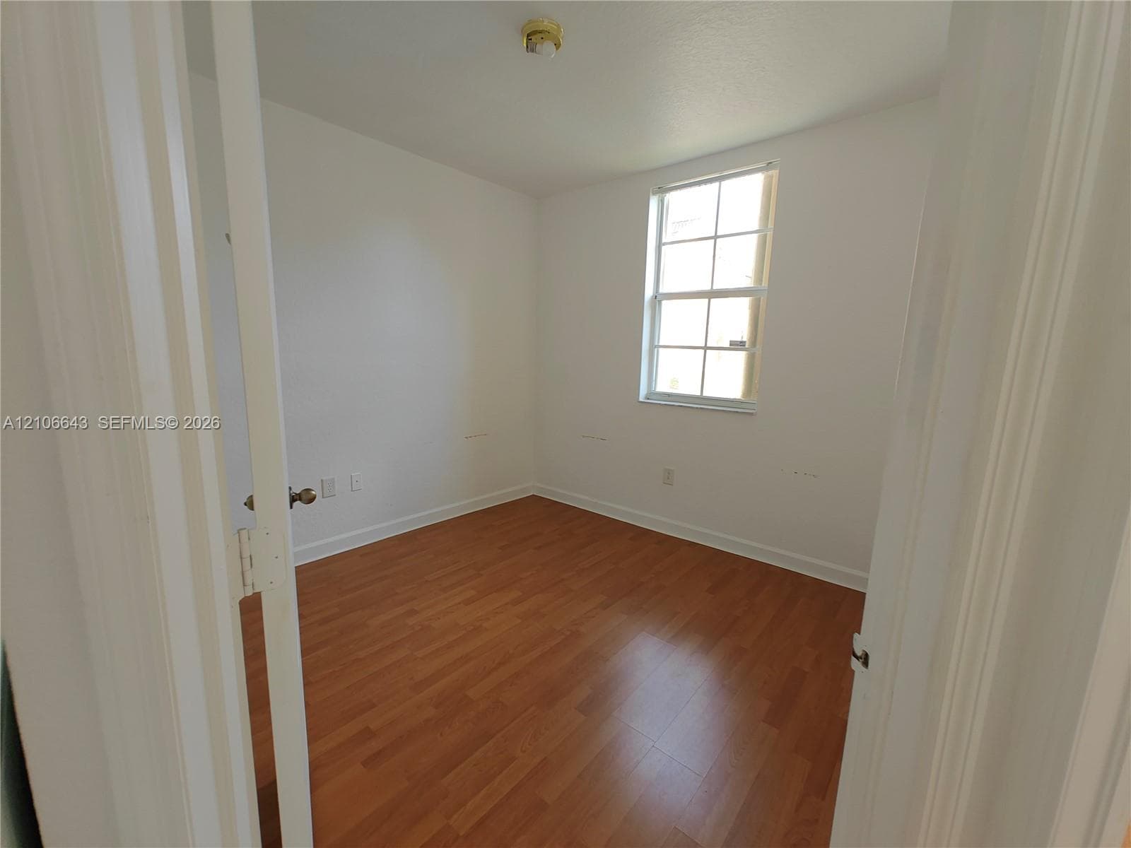 Room featuring wood-finish flooring, white walls, and a window with a multi-pane grid