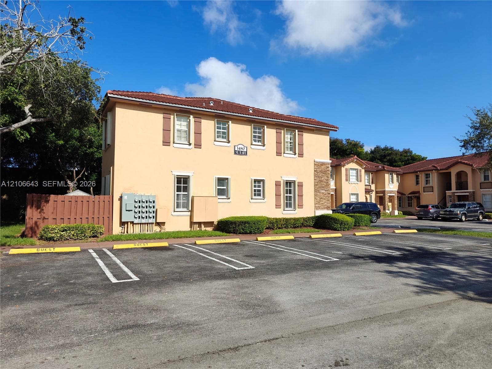 Exterior facade featuring stucco siding, tile roofing, and decorative shutters, with designated guest parking and manicured landscape shrubbery