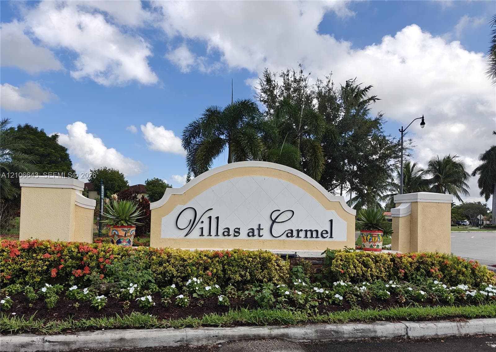 Community entrance monument featuring masonry construction, stucco finish, and detailed landscaping with flowering shrubs and palm trees