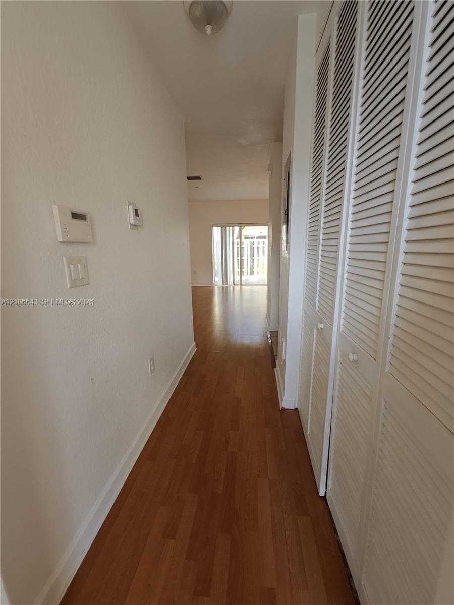 Hallway featuring wood-finish flooring, ceiling-mounted lighting, and built-in white louvered closet doors