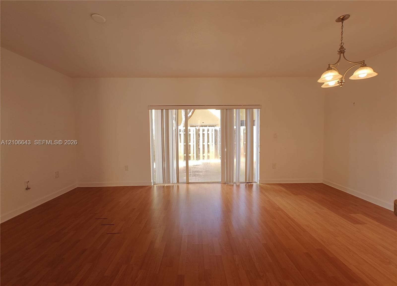 Interior space featuring wood-finish flooring, a multi-light metal chandelier, and a sliding glass door with vertical blinds