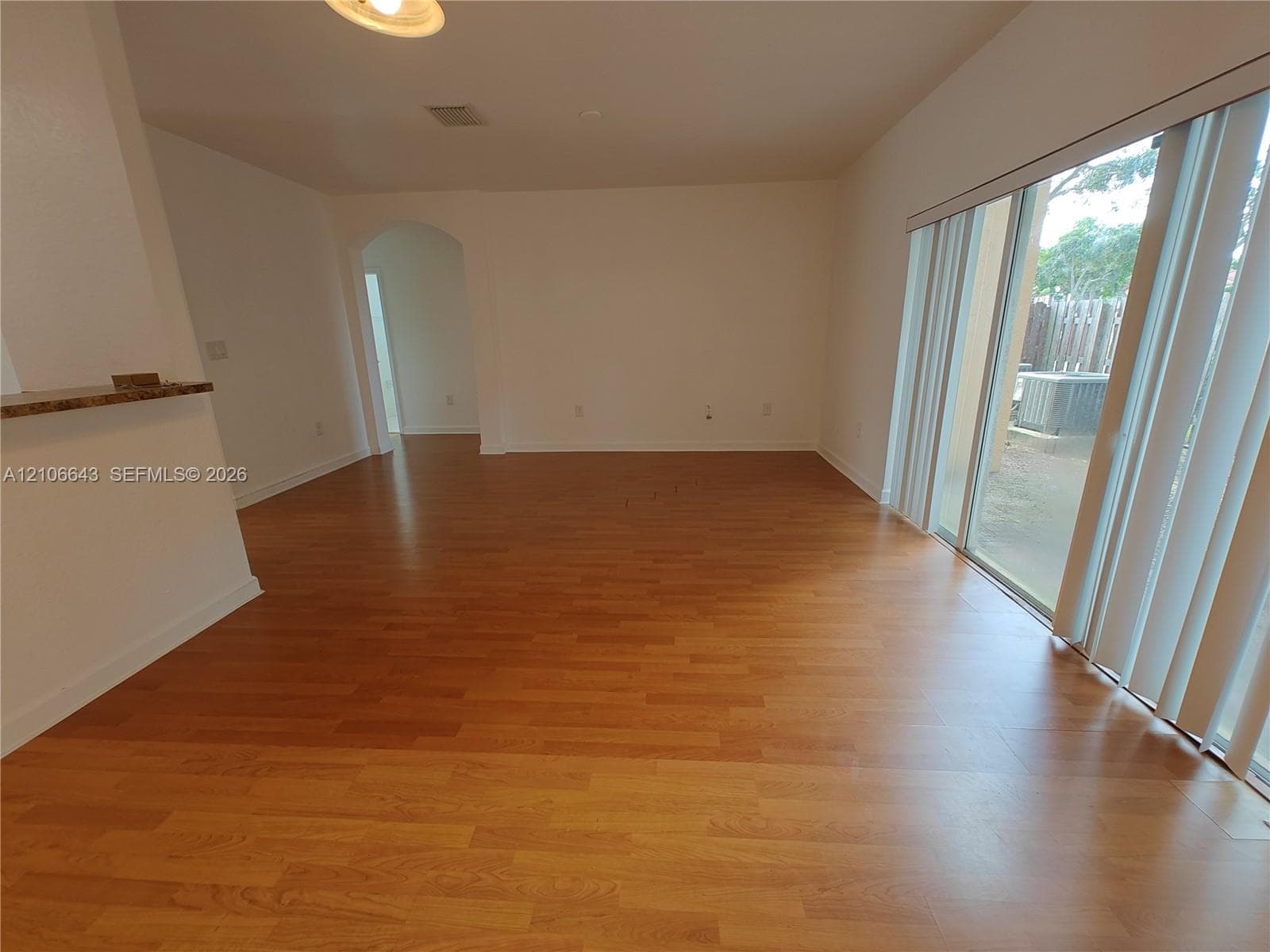 Interior space featuring wood-finish flooring, a neutral color palette, an arched doorway, and large glass sliding doors