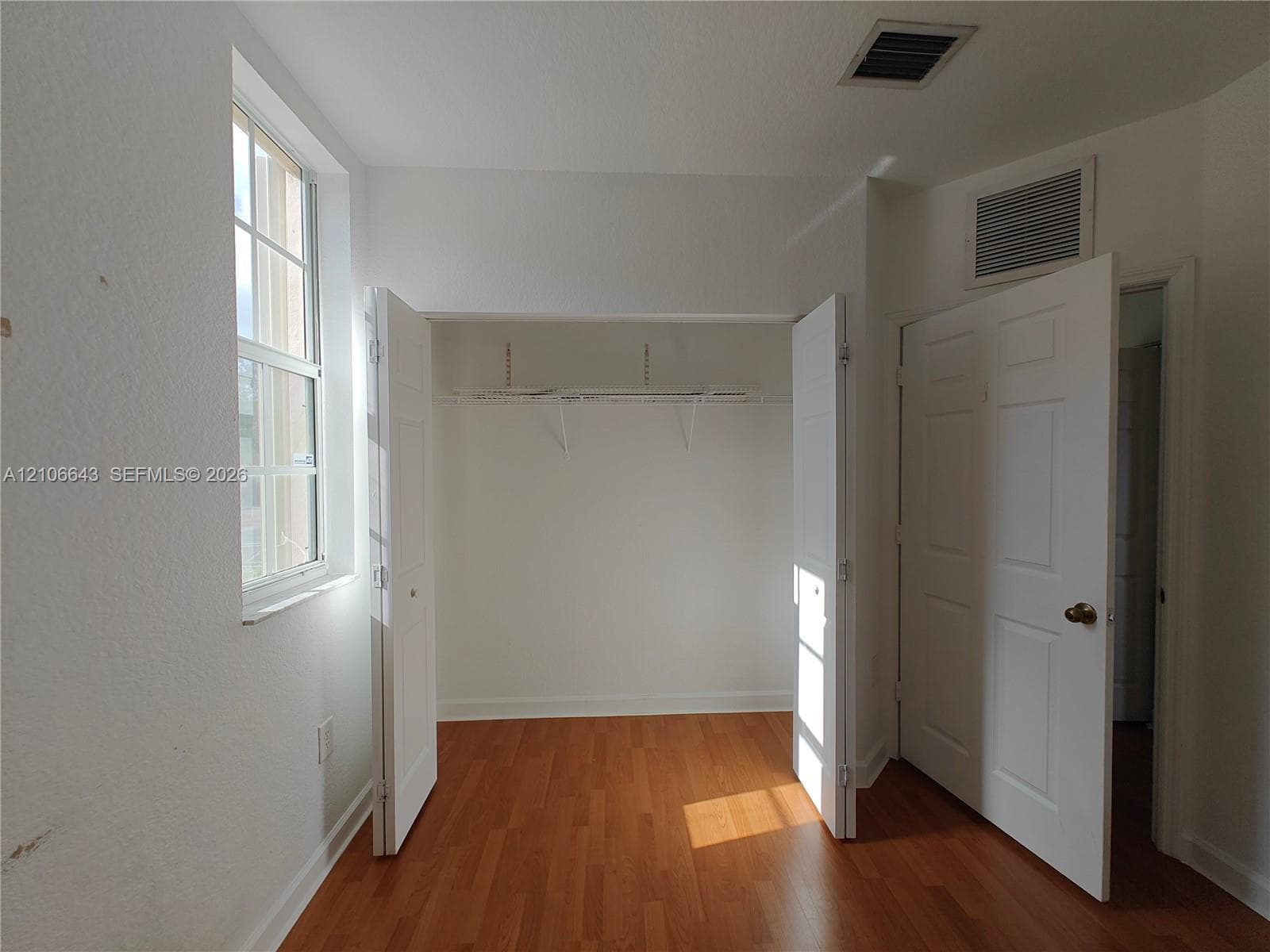Wood-finish flooring, multi-pane window, built-in closet with shelving, and interior panel doors
