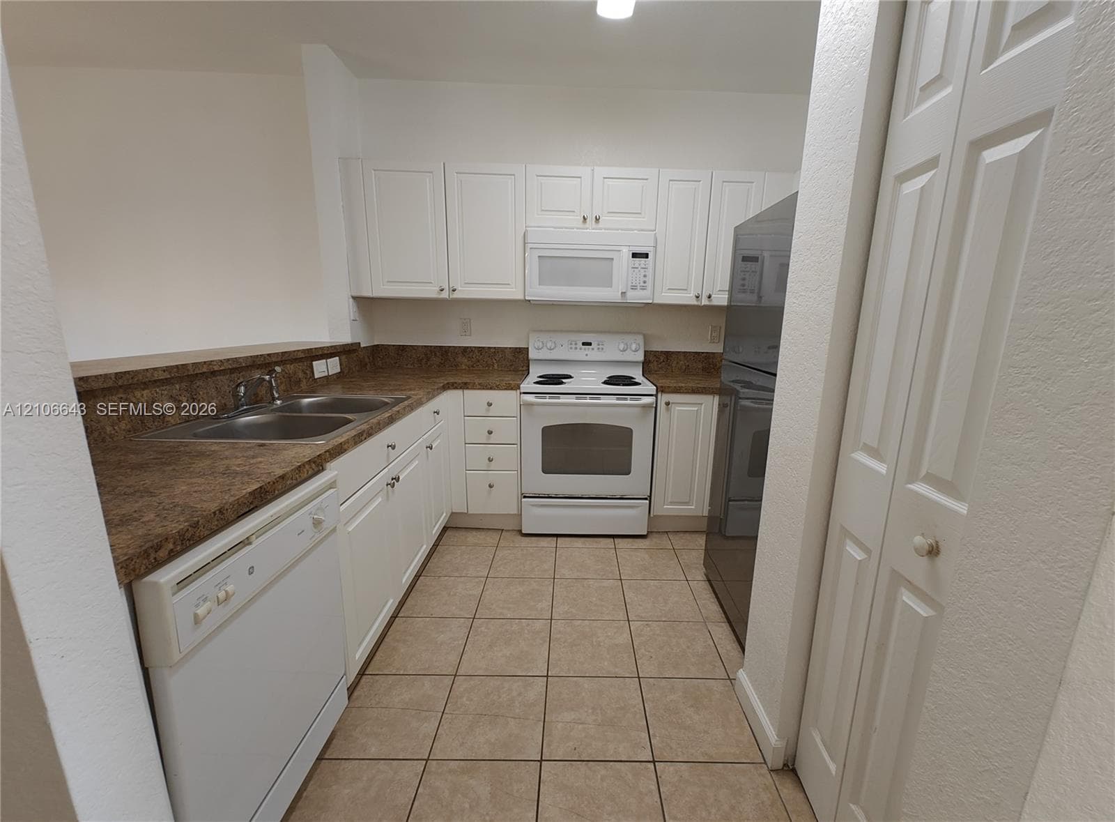 Kitchen featuring white cabinetry, solid-surface countertops, tile flooring, and built-in appliances including a dishwasher, range, and over-the-range microwave
