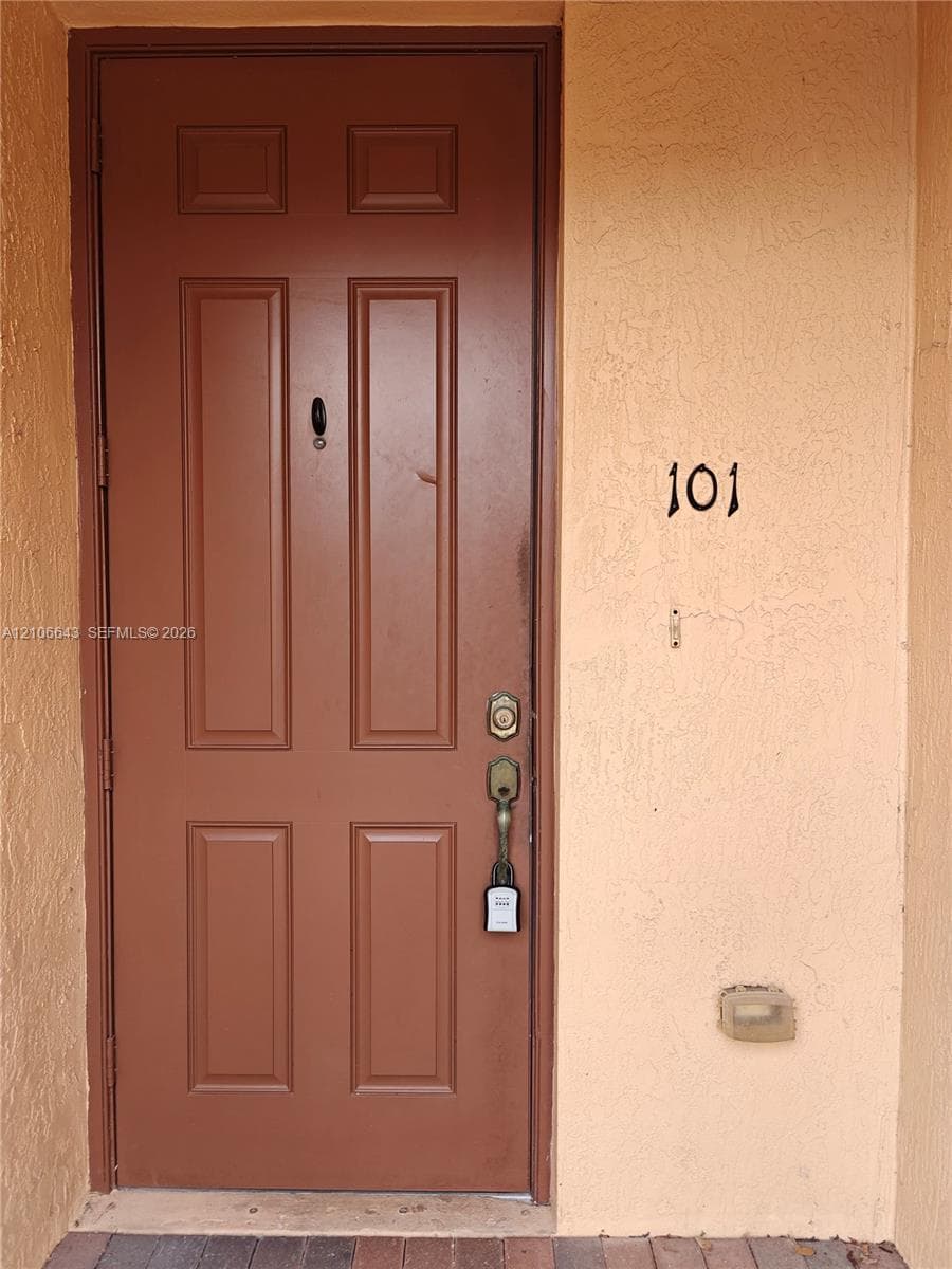 Entryway featuring a four-panel door with a classic peephole, metal lever handle hardware, and a textured stucco exterior finish
