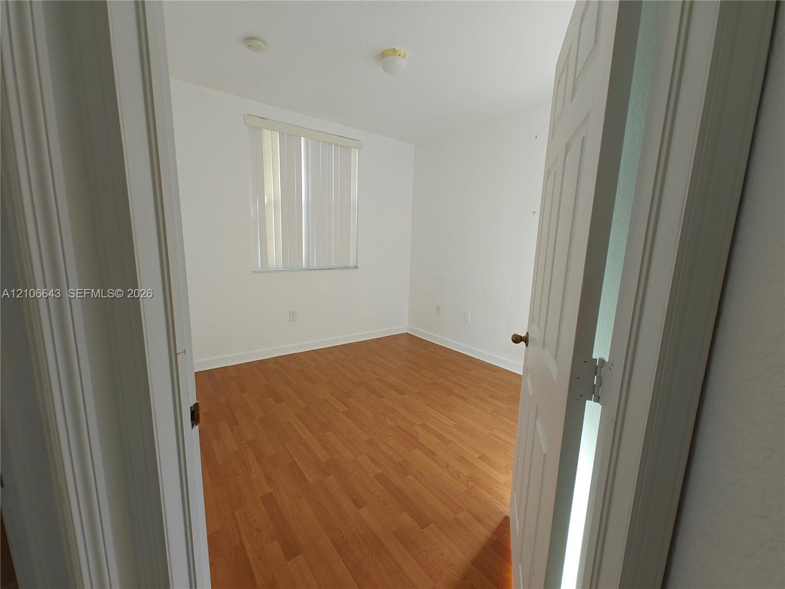 Room featuring wood-finish flooring, white walls, and a window with vertical blinds