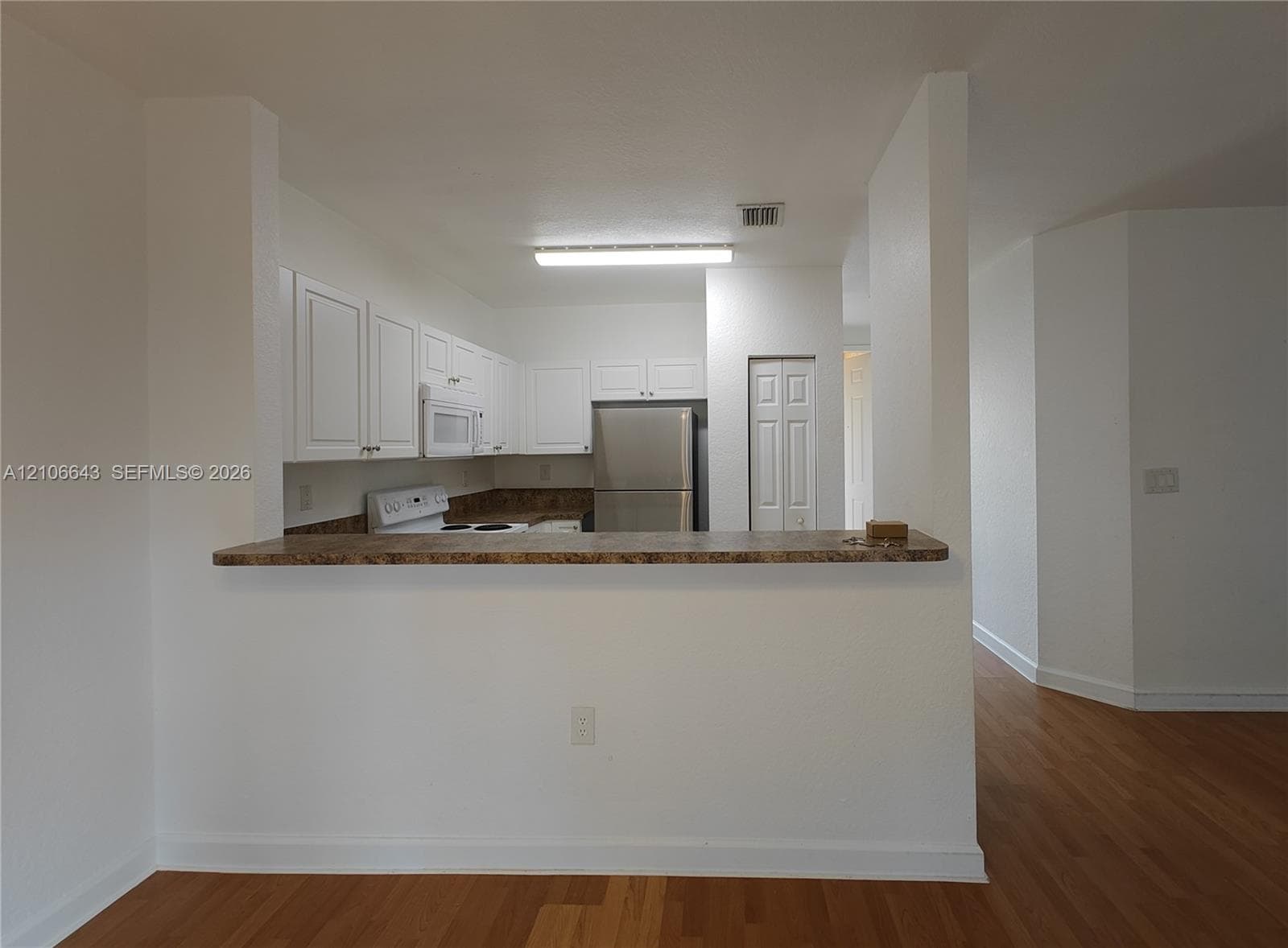 Kitchen featuring white cabinetry, stone-finish countertops, stainless steel refrigerator, and wood-finish flooring