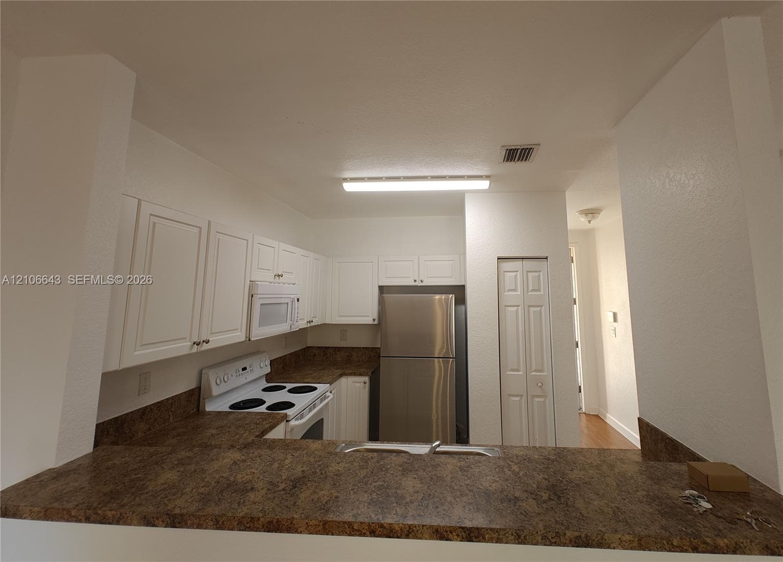 Kitchen featuring white cabinetry, solid-surface countertops, a stainless steel refrigerator, a built-in microwave, and a double-door pantry
