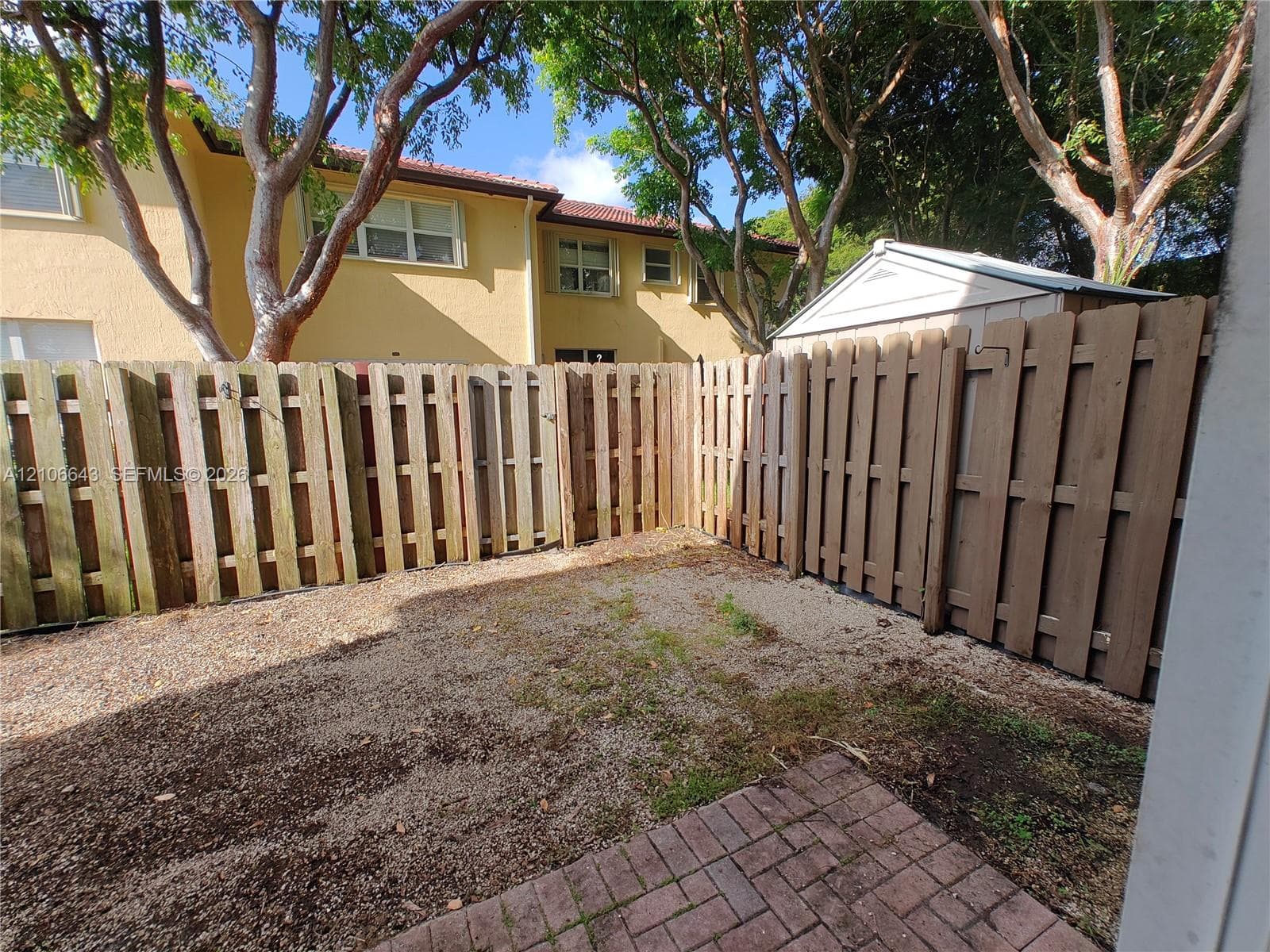 Fenced rear yard featuring a brick paver patio and mature trees