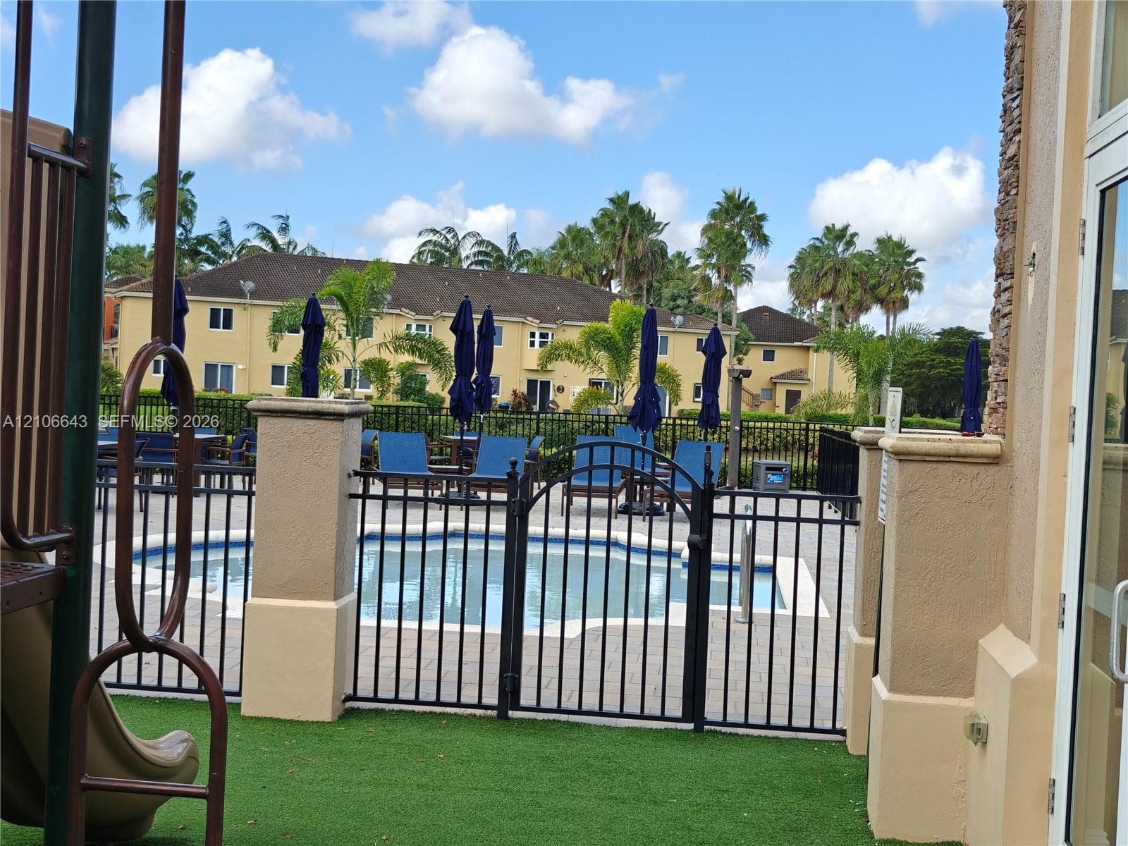 Swimming pool enclosed by black metal fencing, integrated hardscaping, and surrounding tropical landscaping