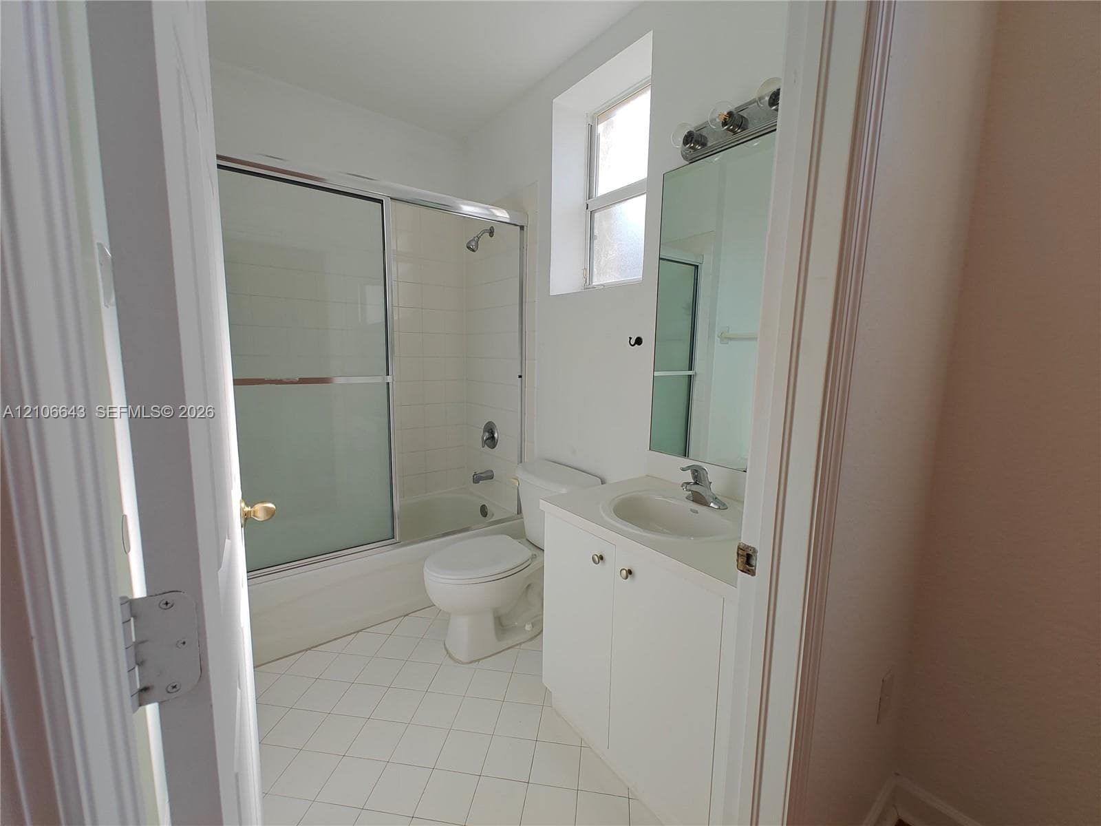 Bathroom featuring tile flooring, a tub-shower combination with a sliding glass door, a vanity with a recessed basin, and a wall-mounted mirror