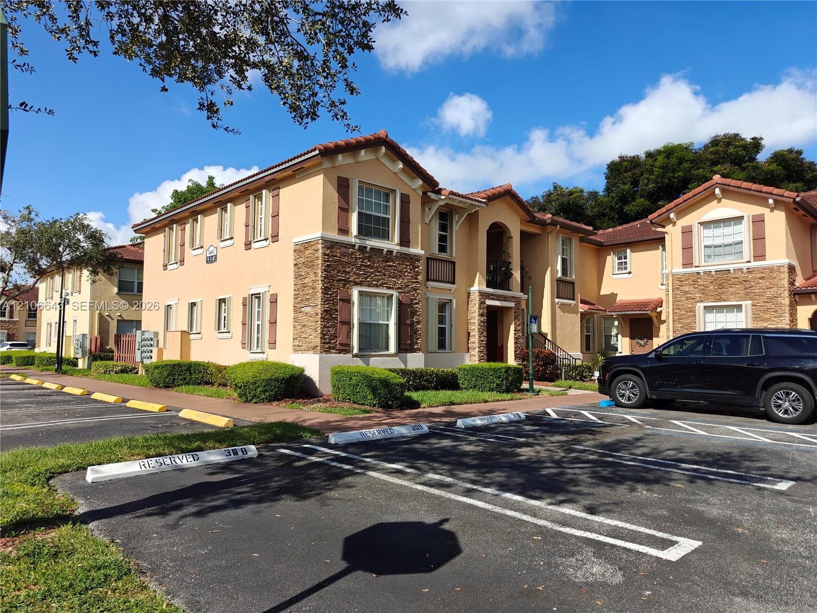 Stucco and stone veneer exterior featuring a tile roof, decorative shutters, and paved parking lot