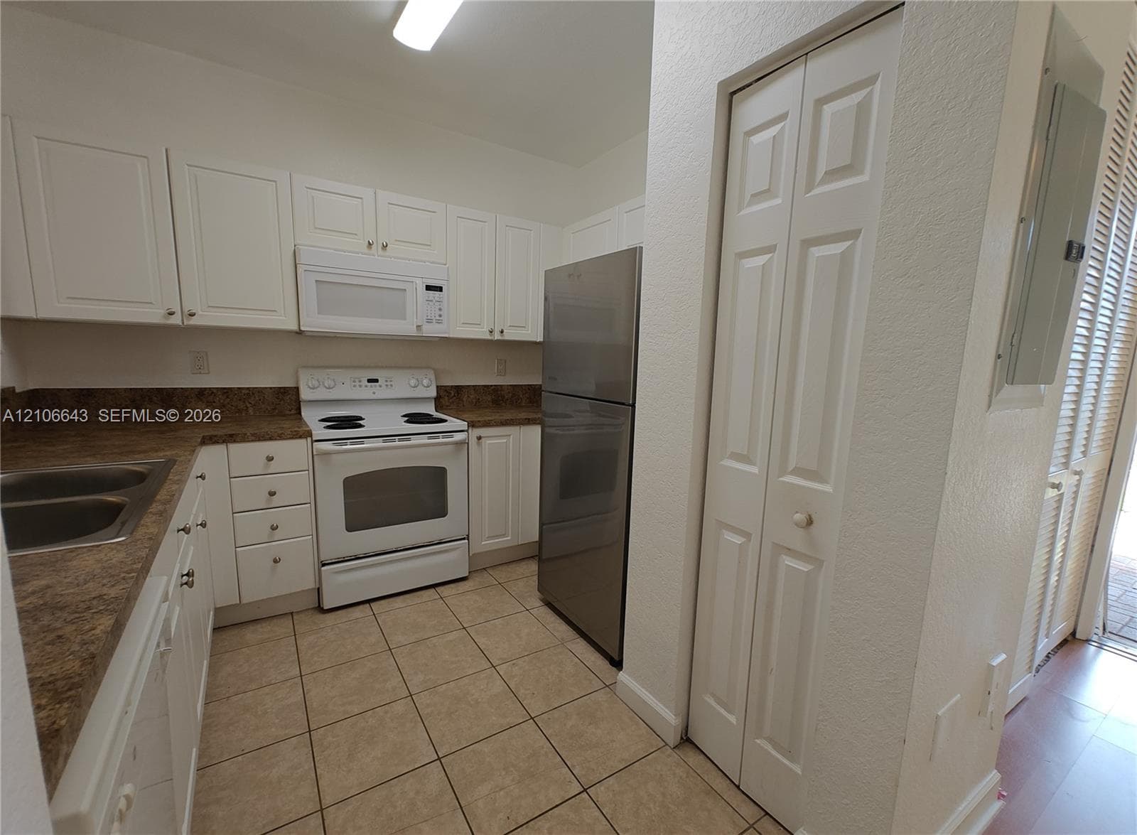 Kitchen featuring white cabinetry, stone-patterned laminate countertops, ceramic tile flooring, stainless steel refrigerator, and integrated white appliance suite