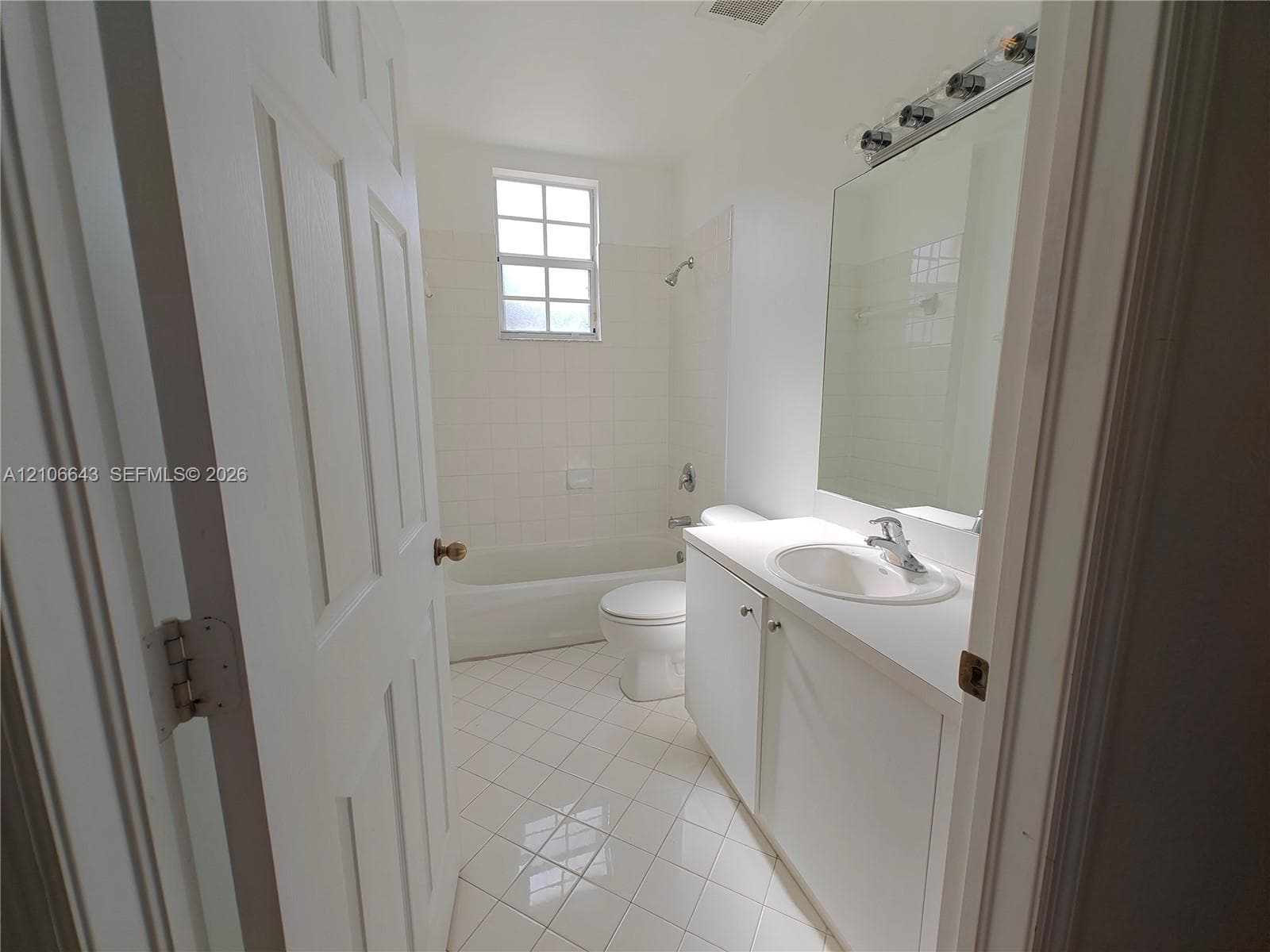 Bathroom featuring a vanity with a white countertop and oval sink, a wall-mounted mirror with integrated lighting, a tub and shower combination with tile surround, and diamond-pattern tile flooring