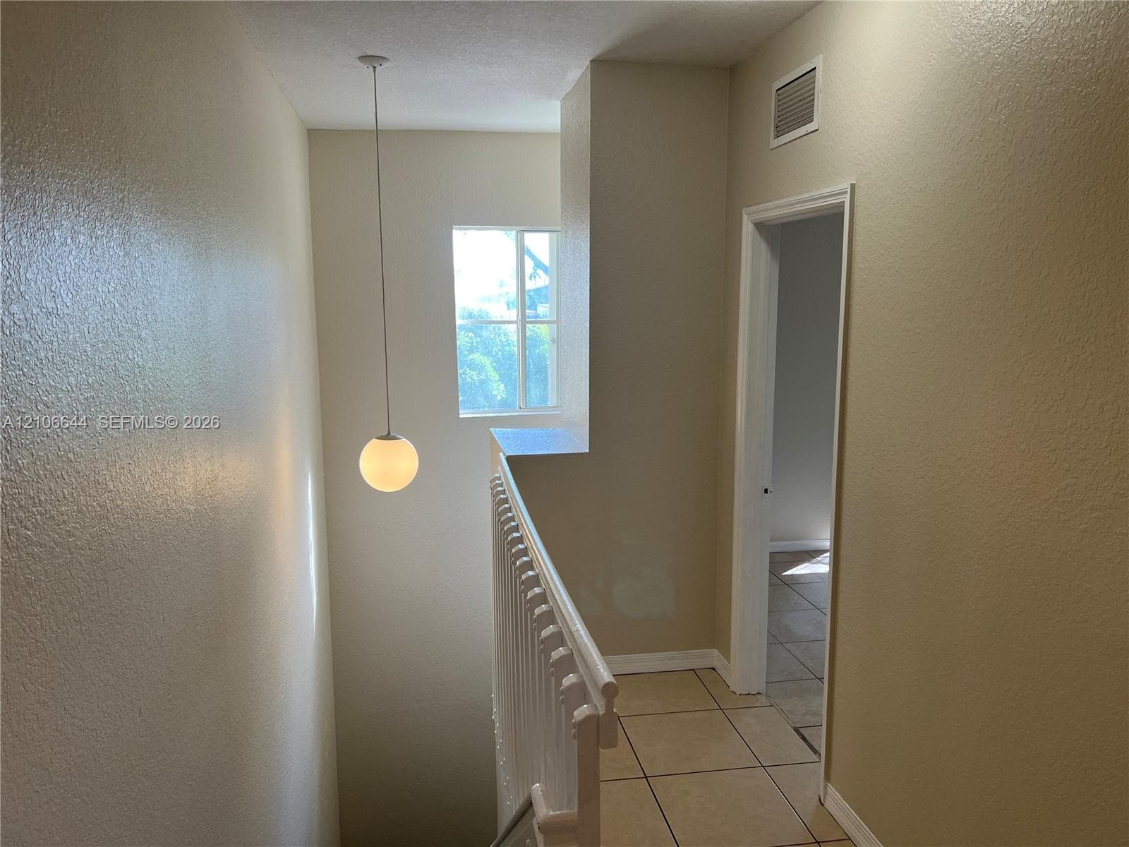 Neutral-toned interior hall featuring white ceramic tile flooring, a spherical pendant light fixture, a square window, and a white balustrade railing